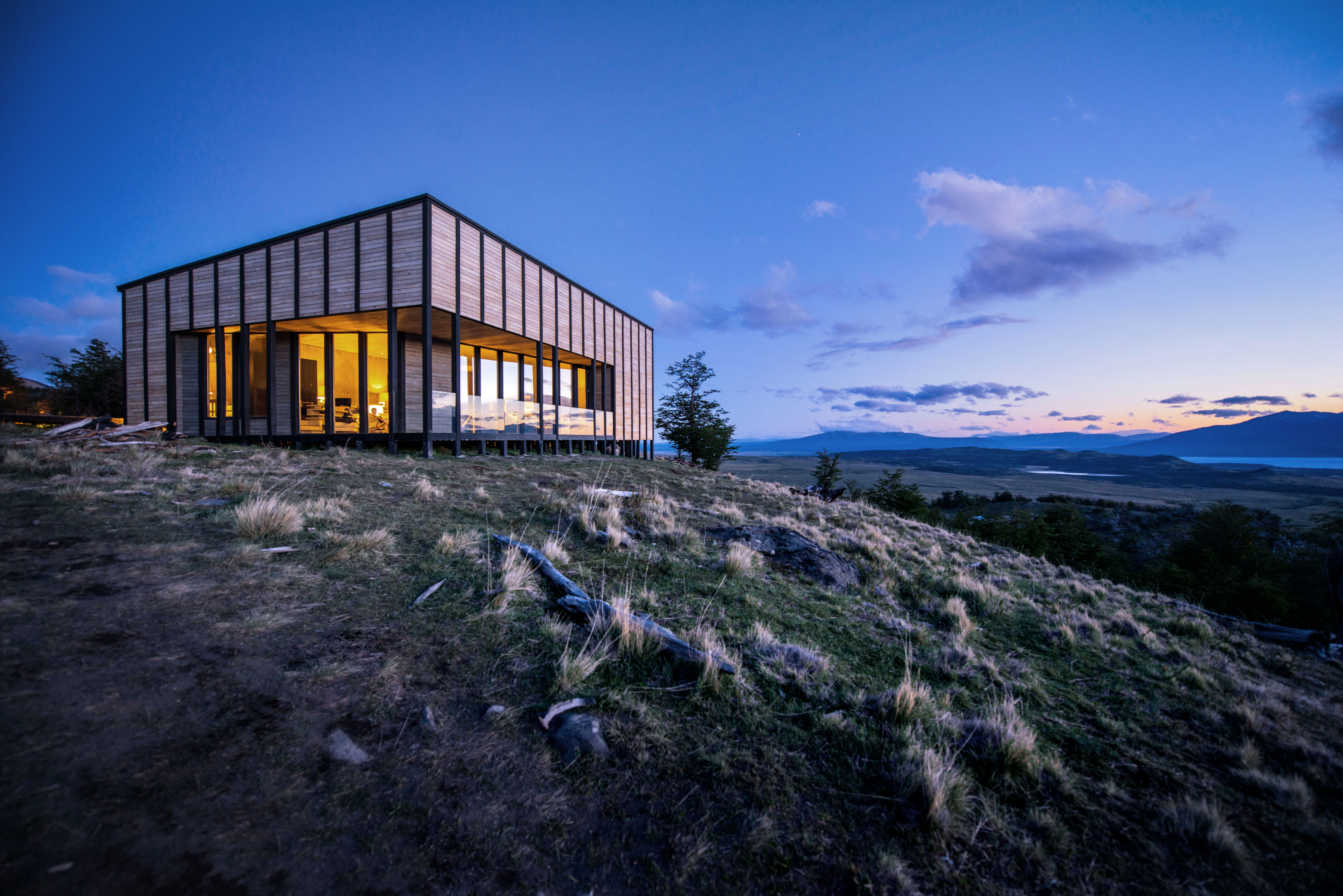 Awasi Patagonia's main lodge glows at dusk on a rocky ridge, its warm windows facing the distant steppe, in Patagonia..