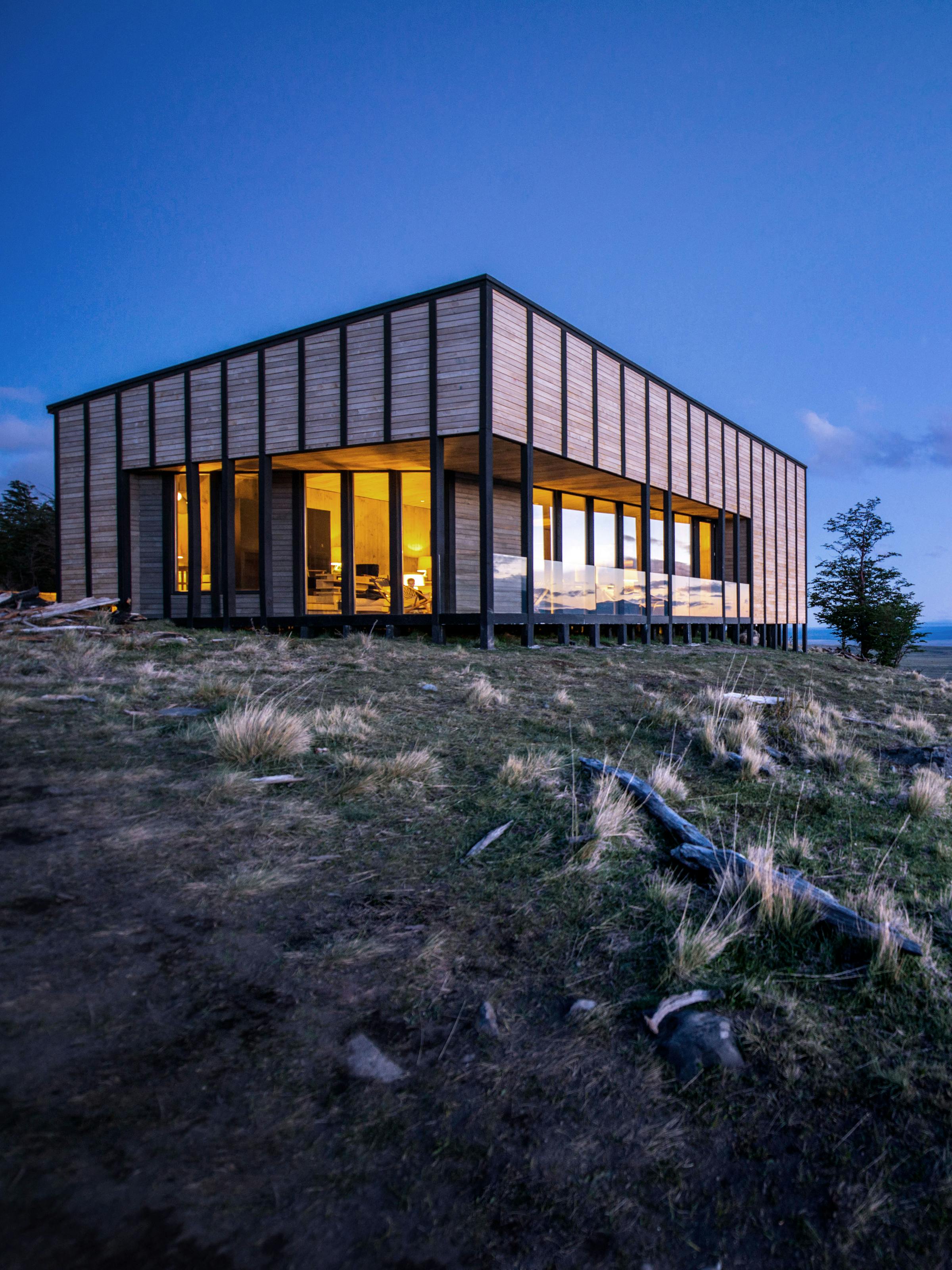 Awasi Patagonia's main lodge glows at dusk on a rocky ridge, its warm windows facing the distant steppe, in Patagonia..