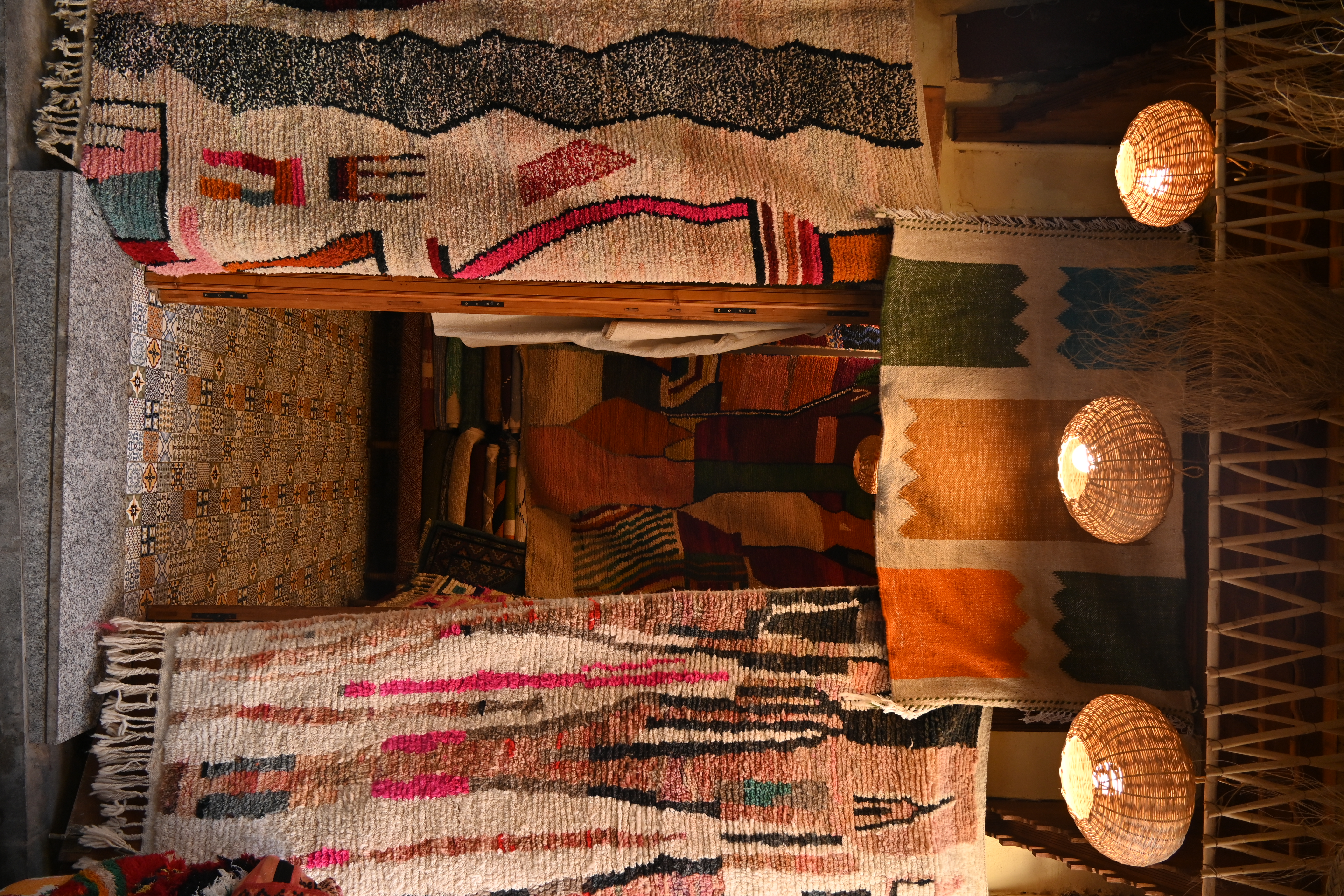Colorful rugs hang at a medina shop entrance, framing a narrow doorway lined with patterned textiles and lanterns.