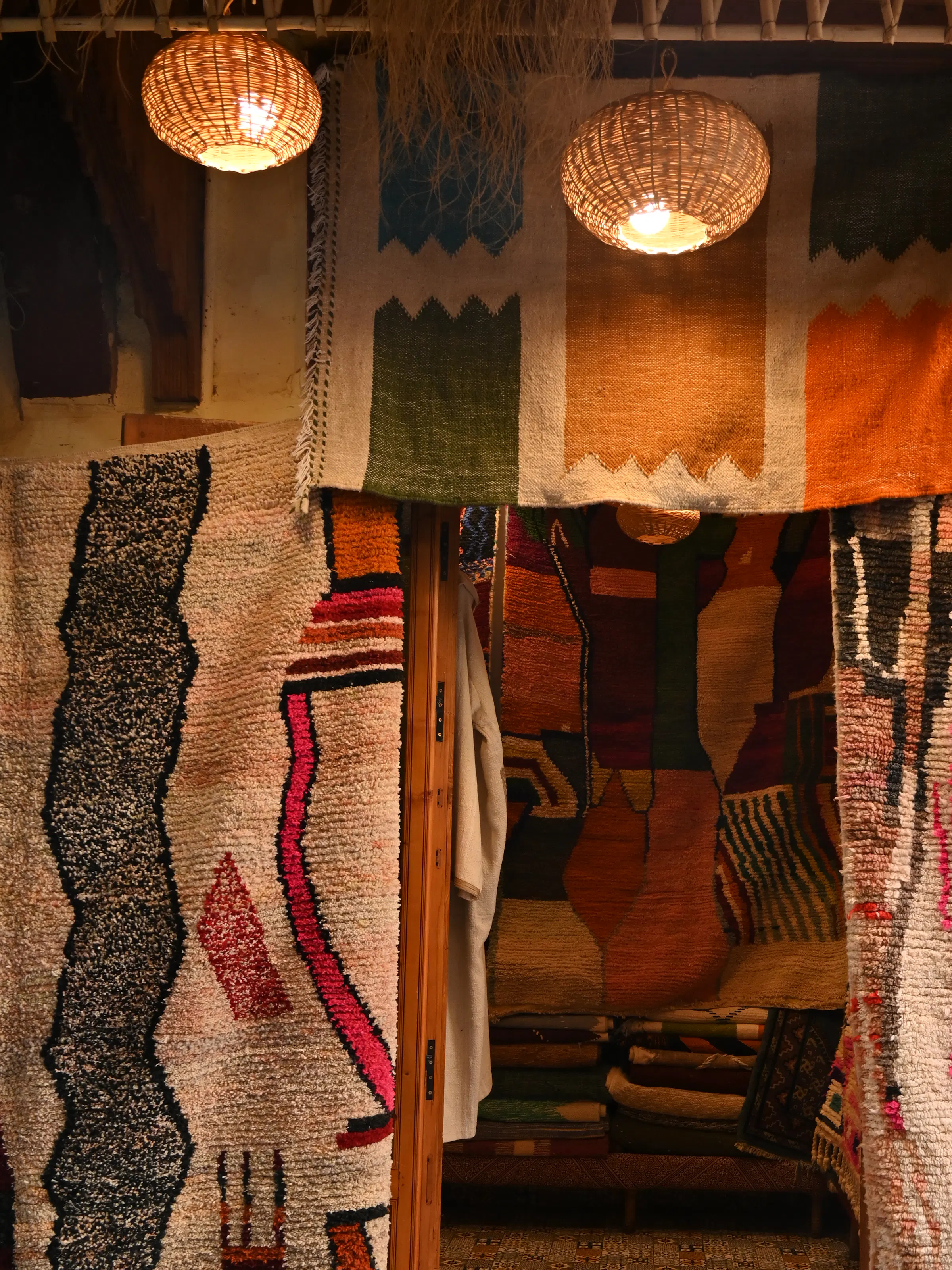 Colorful rugs hang at a medina shop entrance, framing a narrow doorway lined with patterned textiles and lanterns.