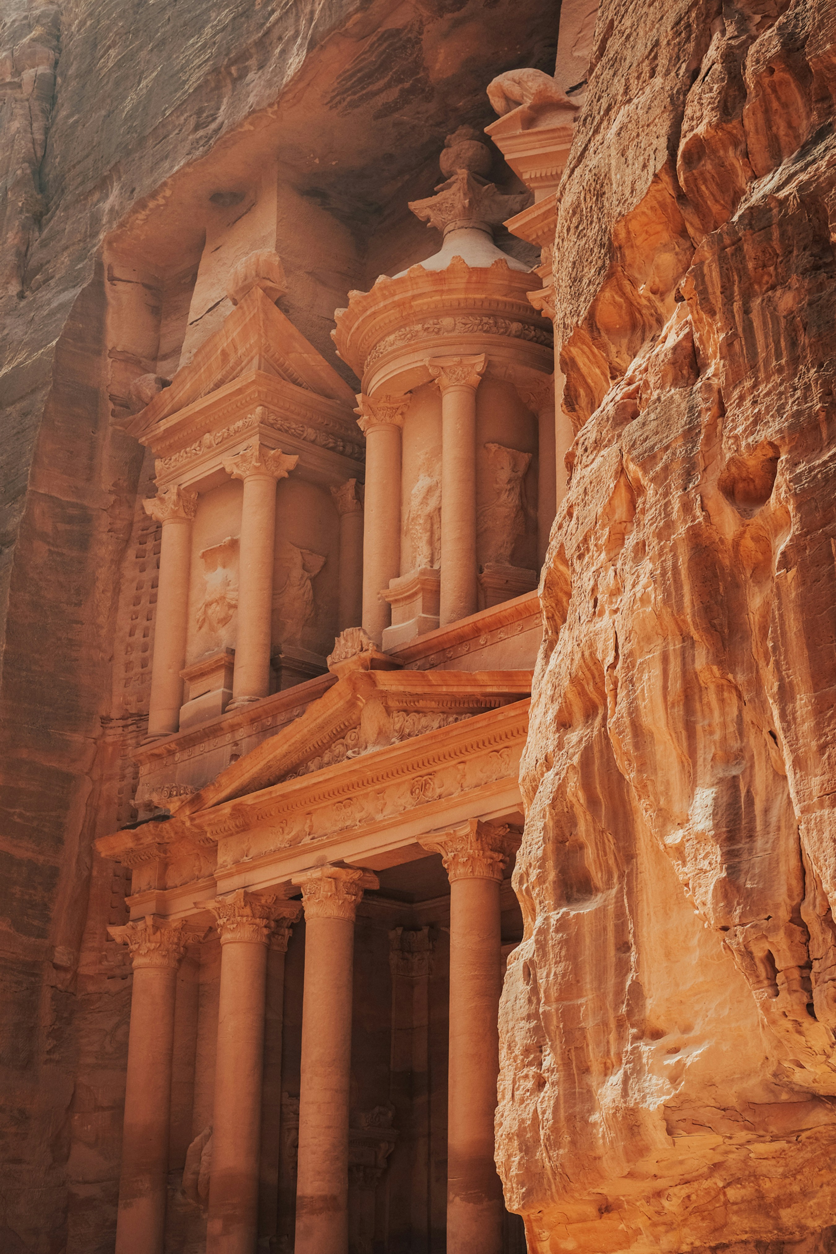 Petra's Treasury appears through the narrow Siq opening, glowing in sunlight between tall orange rock walls.