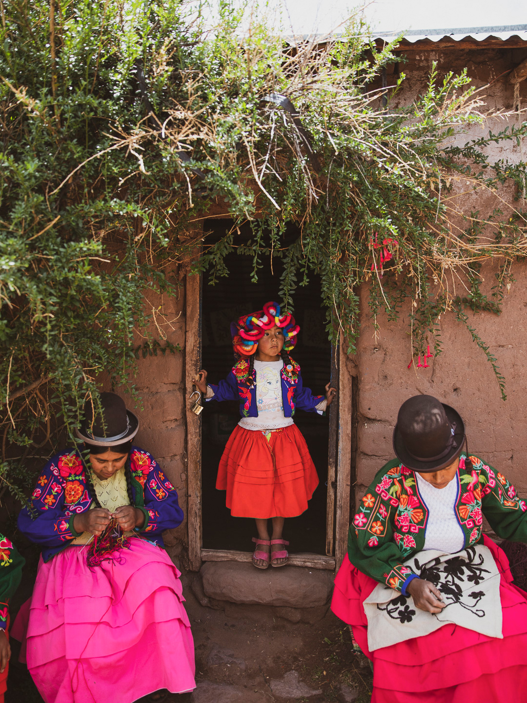 Women in traditional Andean dress and bowler hats cross a stone courtyard, bright skirts catching midday sun.