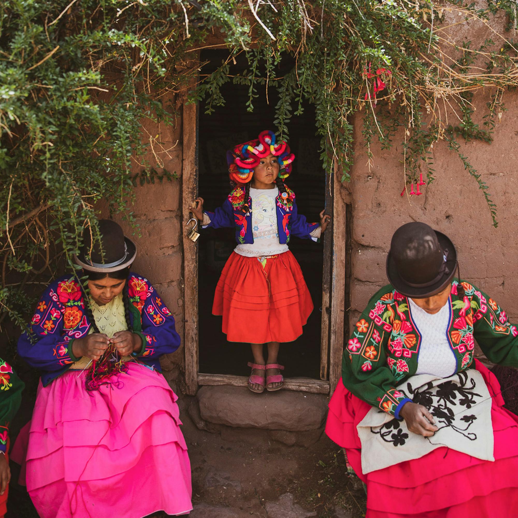 Women in traditional Andean dress and bowler hats cross a stone courtyard, bright skirts catching midday sun.