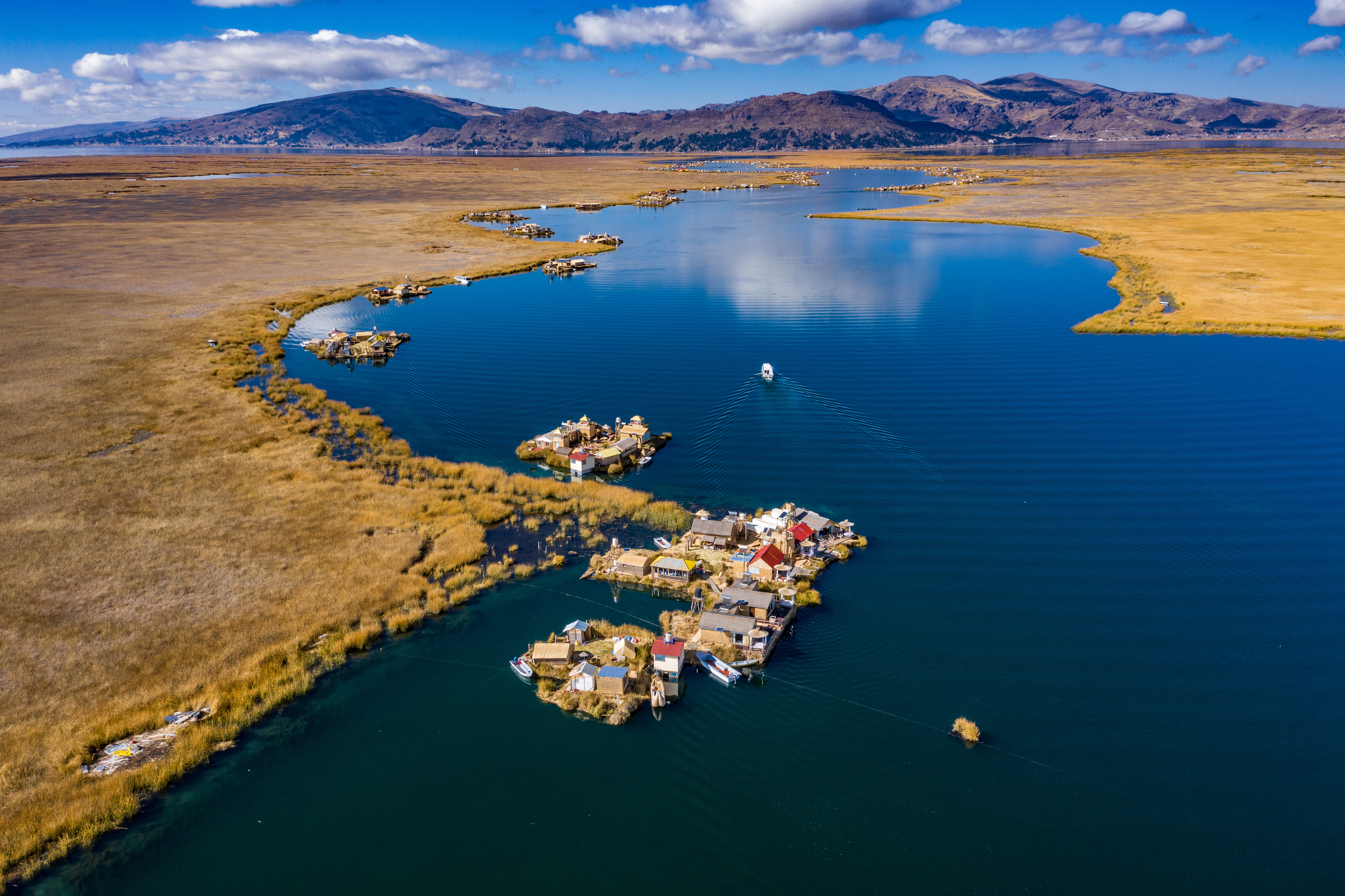 Aerial view of Lake Titicaca shoreline and islands, a small town curving around deep blue water and bays below.