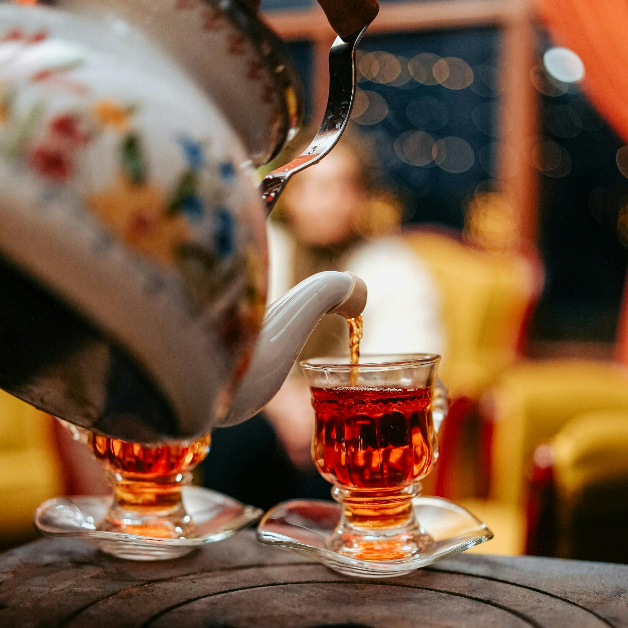 Two glasses of mint tea sit on a café table, amber liquid glowing while a busy market scene blurs behind.