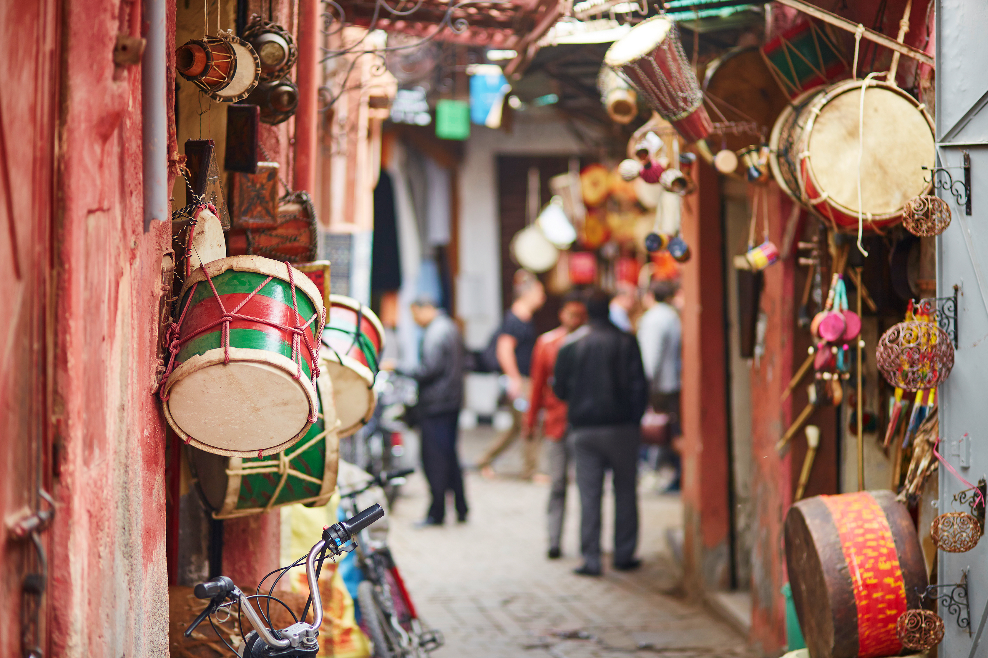 Brightly painted drums hang from a market stall, with lanterns and souvenirs lining the lane behind them.