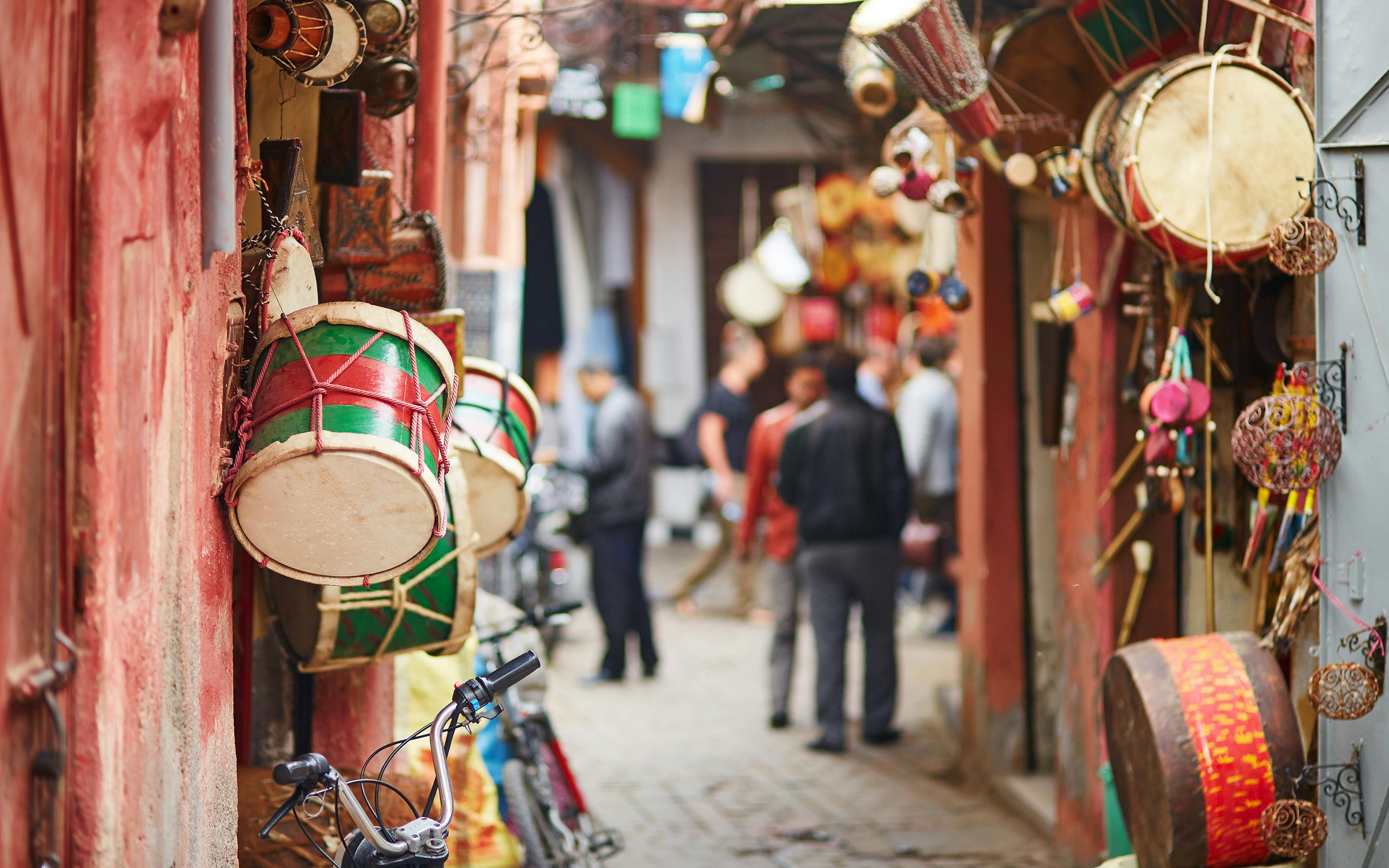 Brightly painted drums hang from a market stall, with lanterns and souvenirs lining the lane behind them.
