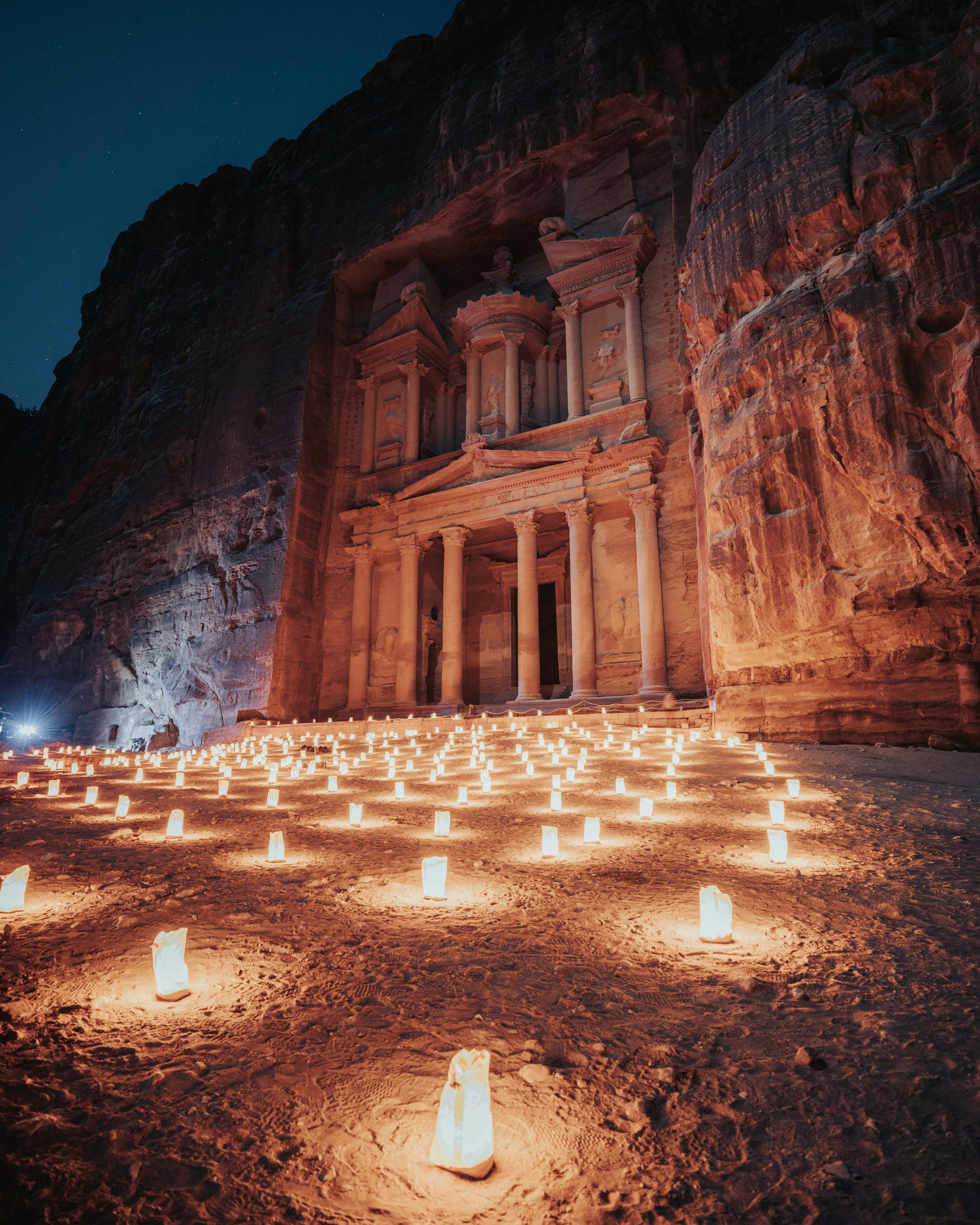 Candles glow in rows leading to Petra's Treasury, the carved facade lit softly against dark sandstone cliffs.