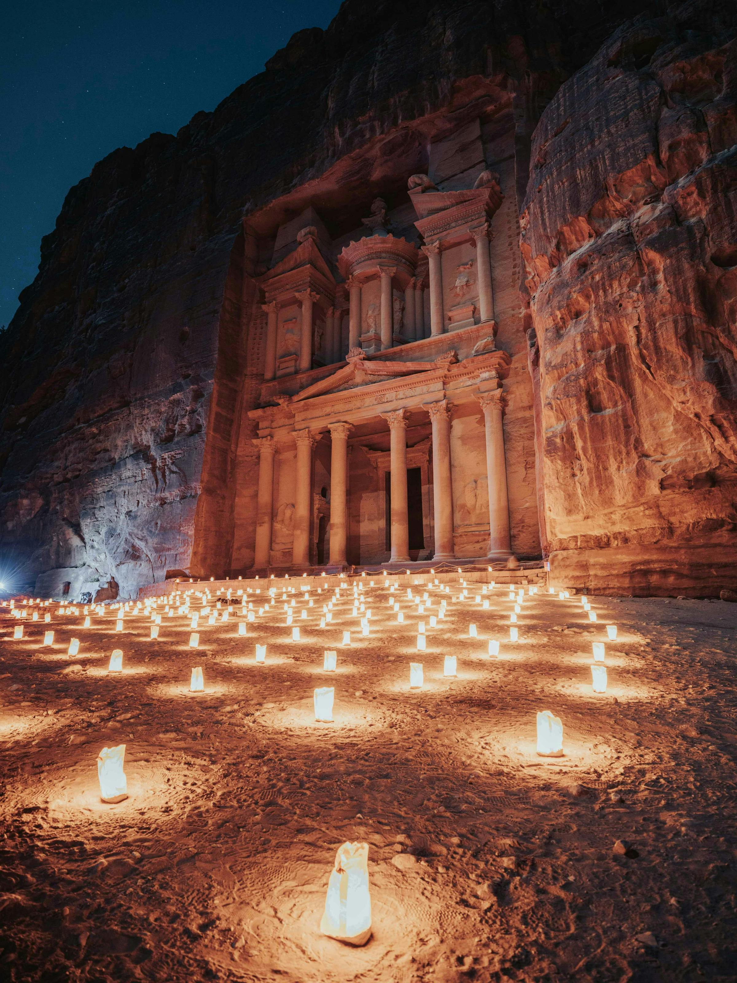 Candles glow in rows leading to Petra's Treasury, the carved facade lit softly against dark sandstone cliffs.