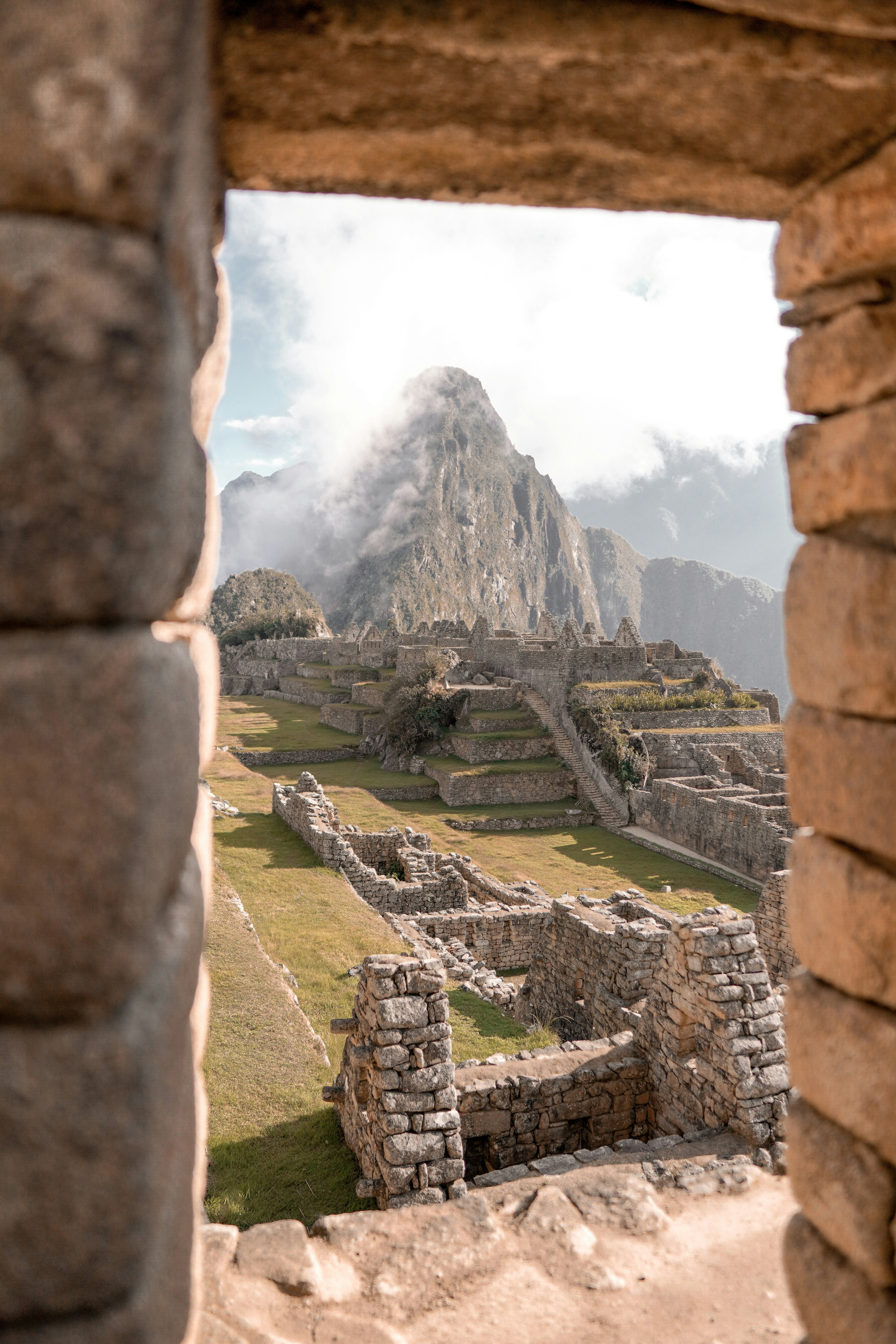 Machu Picchu terraces appear through a stone doorway, framing the ruins and mountains beneath low cloud cover.