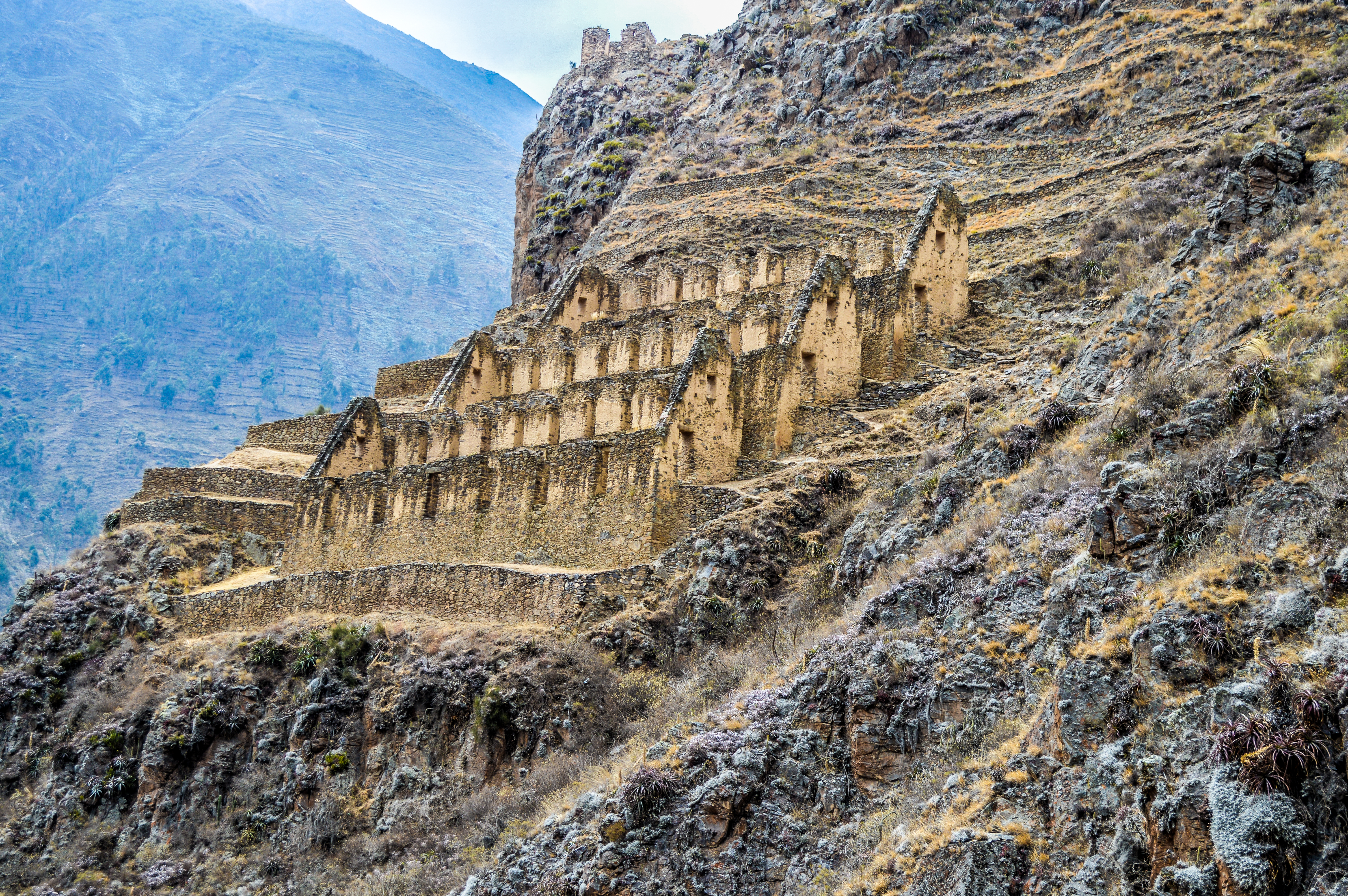Stone terraces and Inca ruins cling to a steep hillside in the Sacred Valley, with rugged mountains behind.