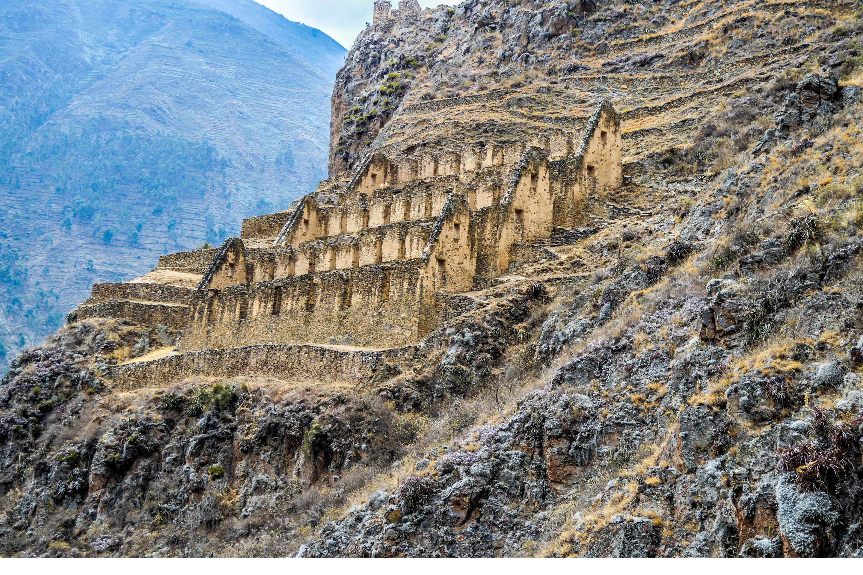 Stone terraces and Inca ruins cling to a steep hillside in the Sacred Valley, with rugged mountains behind.