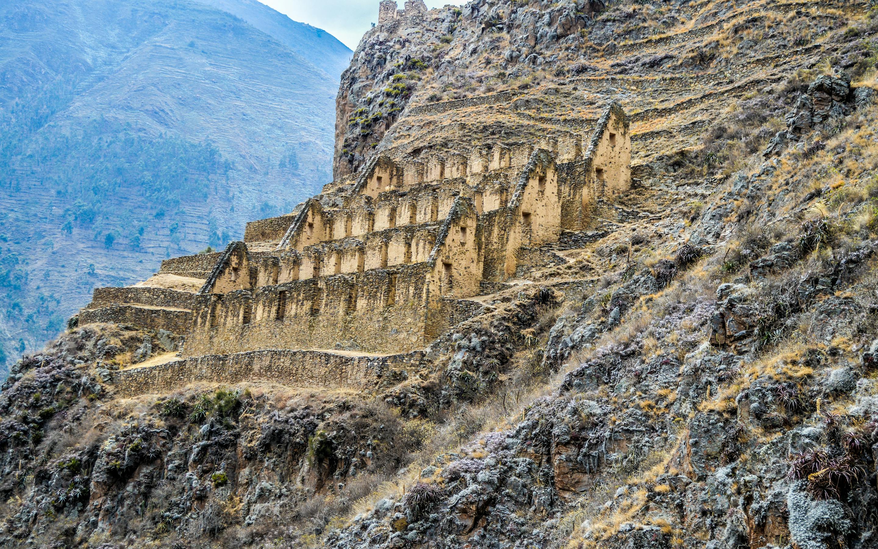 Stone terraces and Inca ruins cling to a steep hillside in the Sacred Valley, with rugged mountains behind.