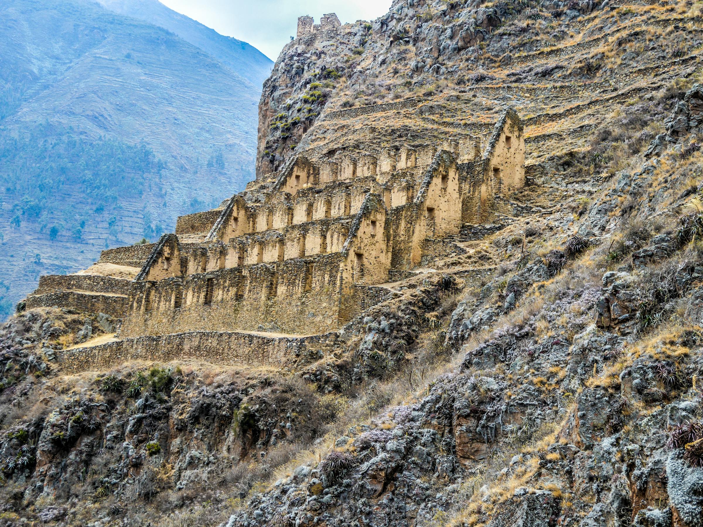 Stone terraces and Inca ruins cling to a steep hillside in the Sacred Valley, with rugged mountains behind.