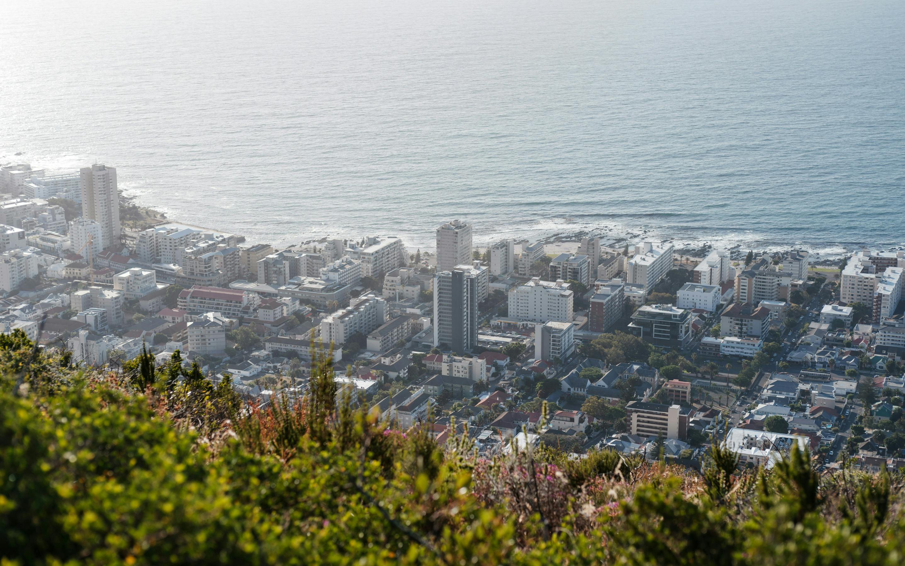 A wide view over Cape Town reveals dense neighborhoods and the Atlantic coastline stretching along the horizon.