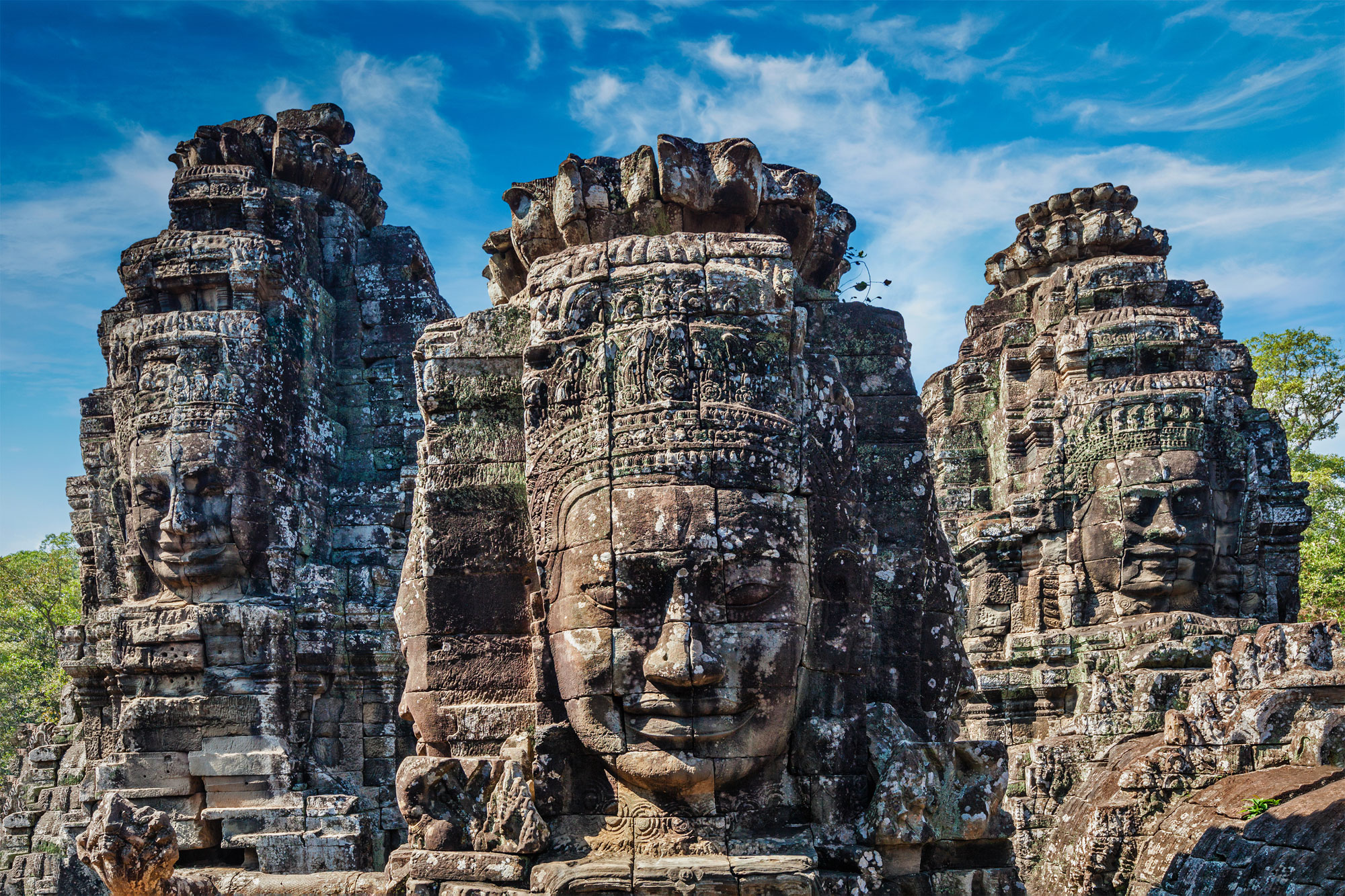 Close-up of the towering stone faces of Bayon Temple, intricately carved and weathered, set against a bright blue sky.