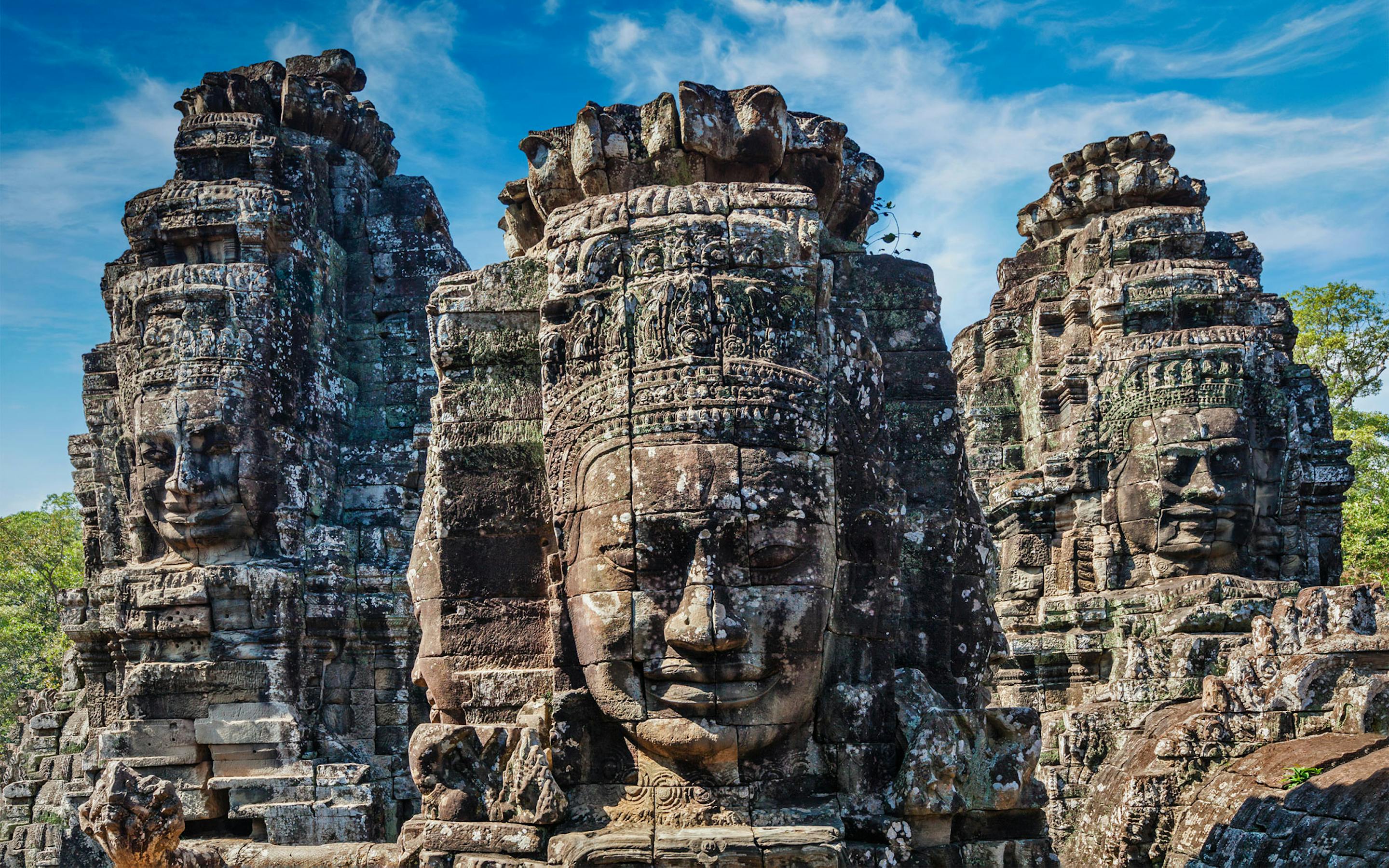 Close-up of the towering stone faces of Bayon Temple, intricately carved and weathered, set against a bright blue sky.