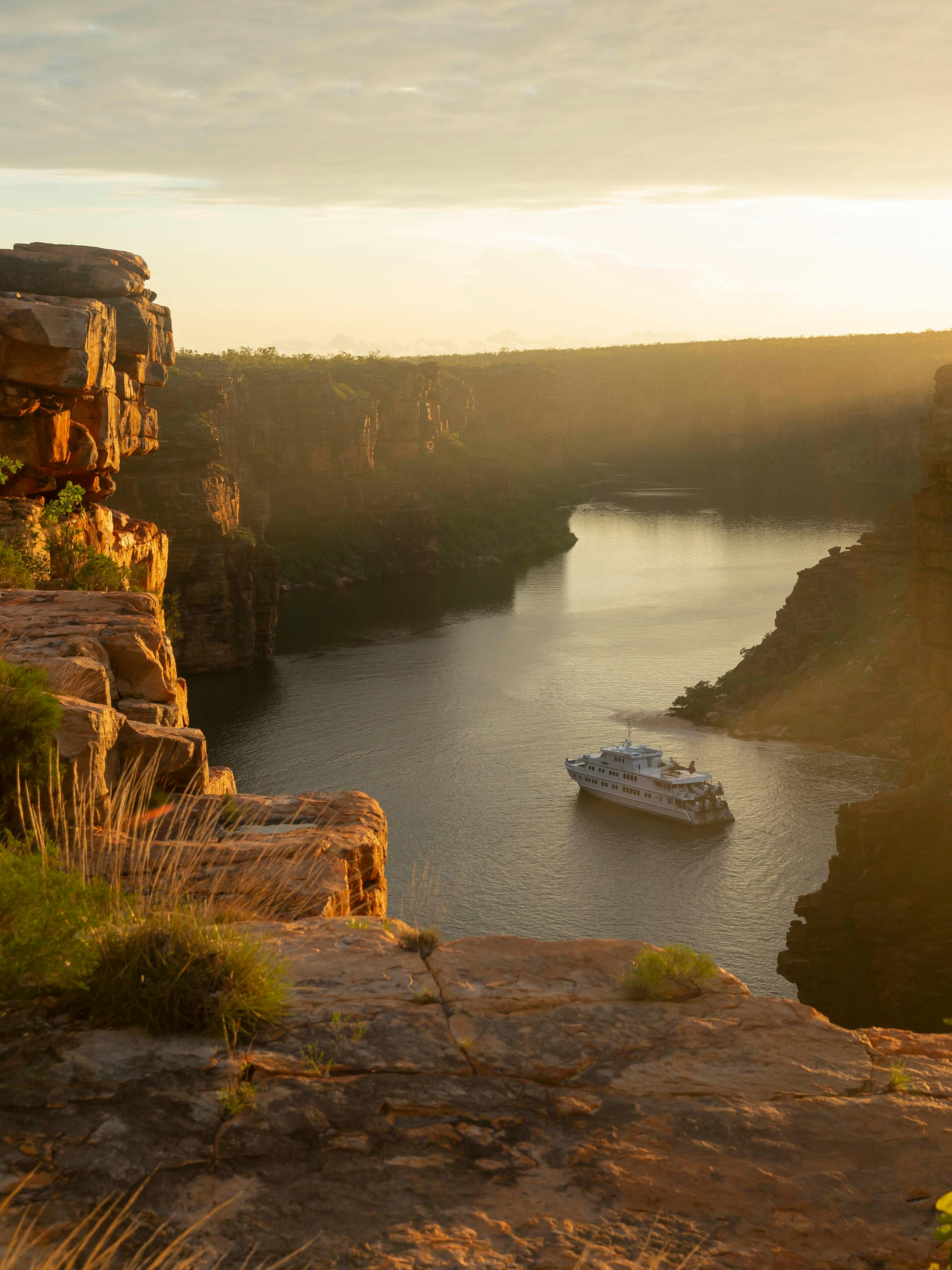 Golden sunset lights a winding river gorge, with rugged cliffs and a small boat traveling through the calm channel.