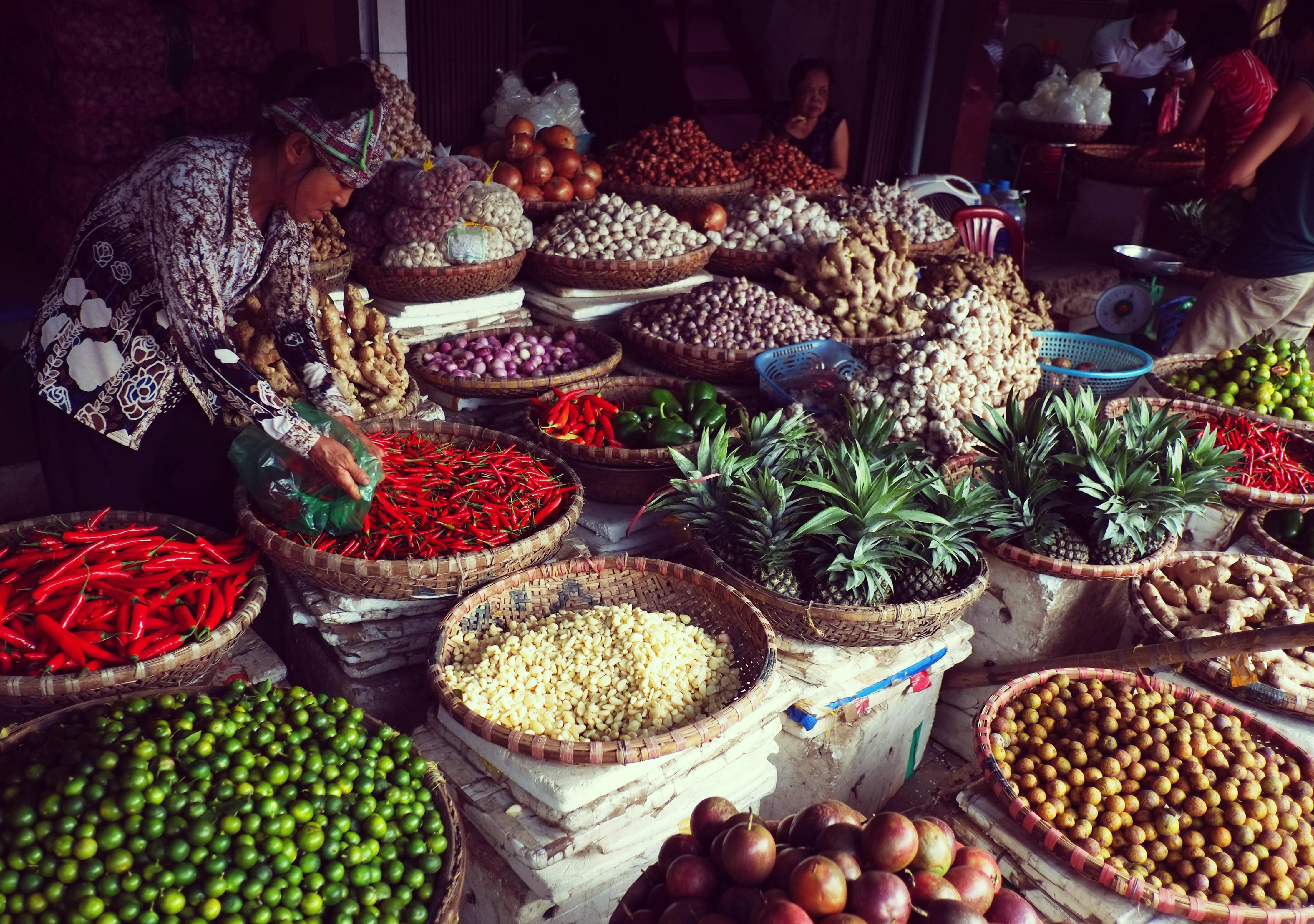 Colorful bowls of chiles, herbs, and fruit fill a Hanoi market stall as a vendor neatly arranges the display.
