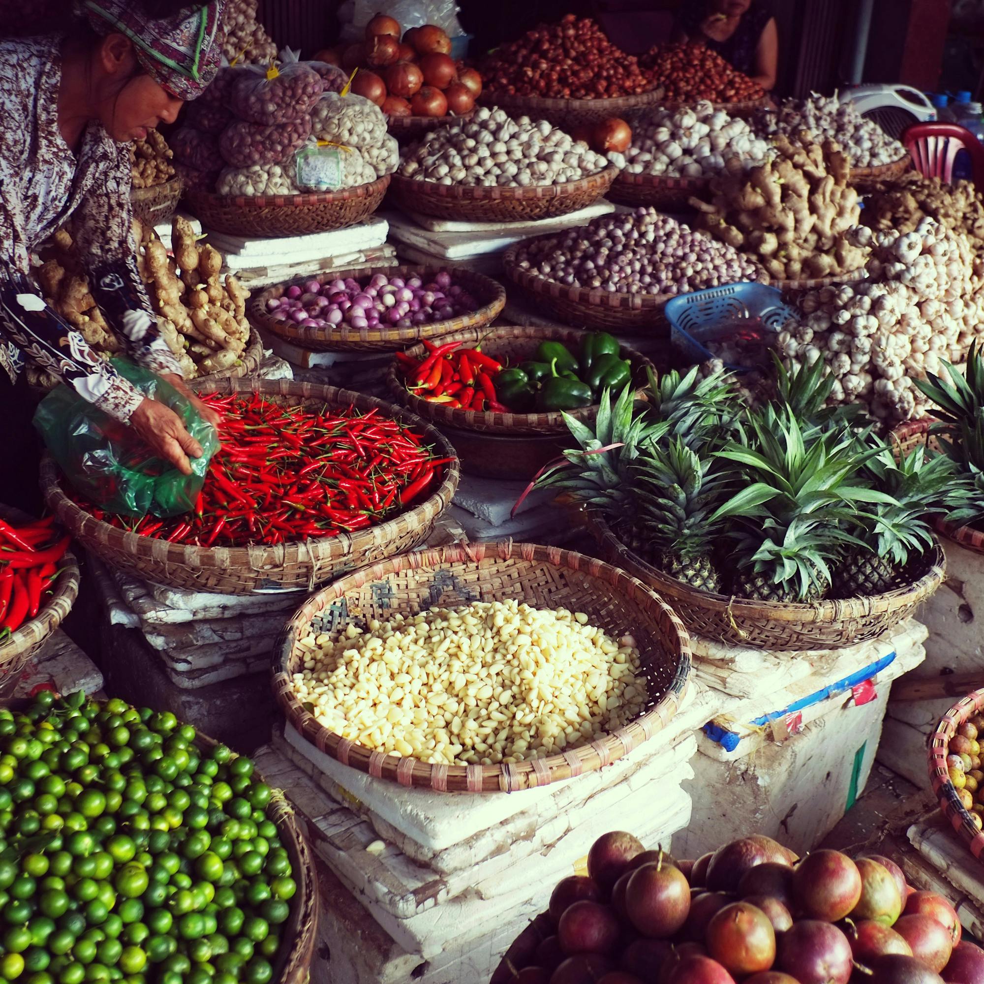 Colorful bowls of chiles, herbs, and fruit fill a Hanoi market stall as a vendor neatly arranges the display.