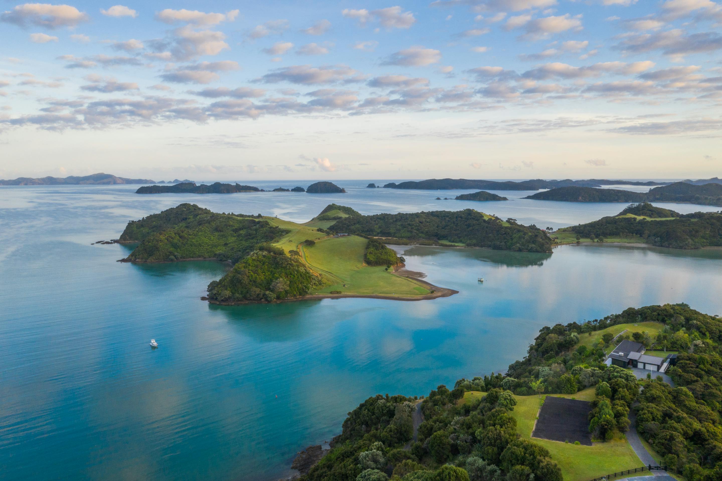 Aerial view of green islands and sheltered bays in bright blue water, dotted with small boats beneath scattered clouds.