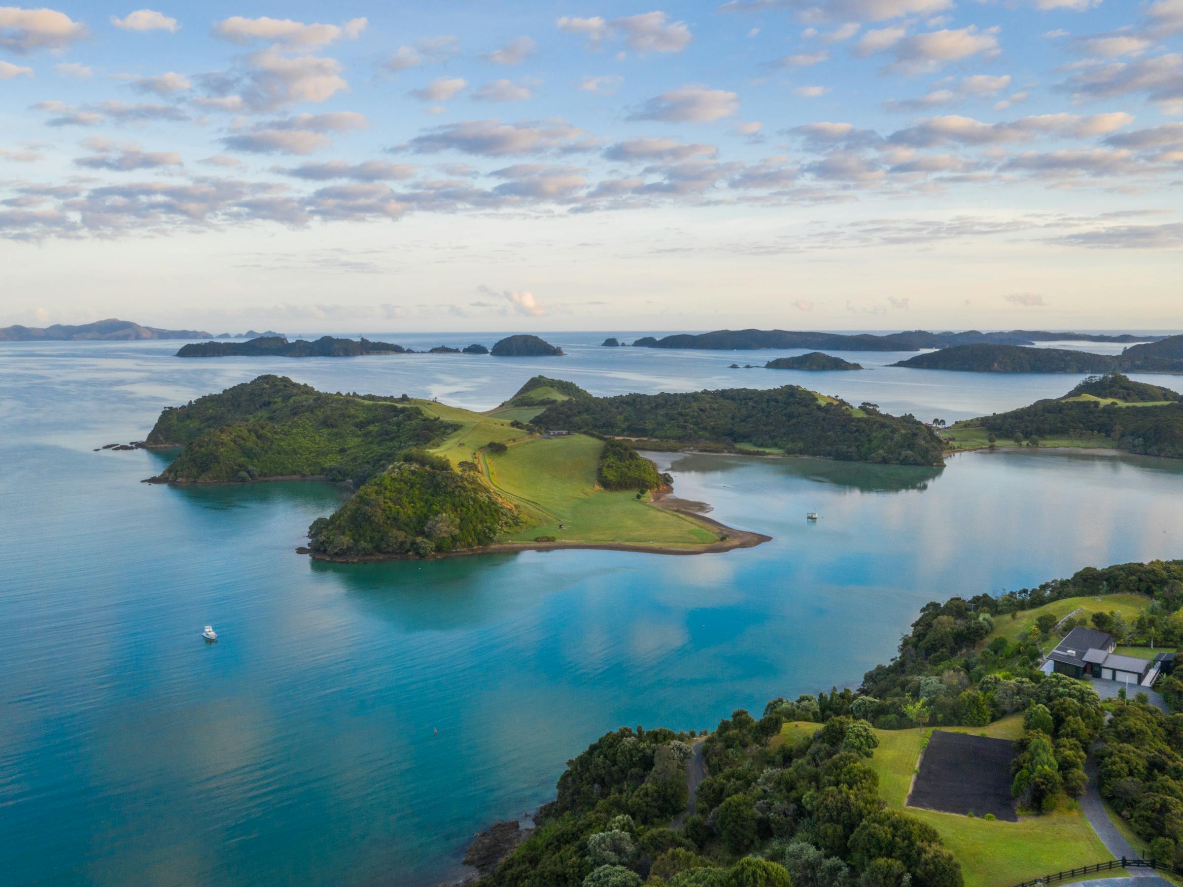 Aerial view of green islands and sheltered bays in bright blue water, dotted with small boats beneath scattered clouds.