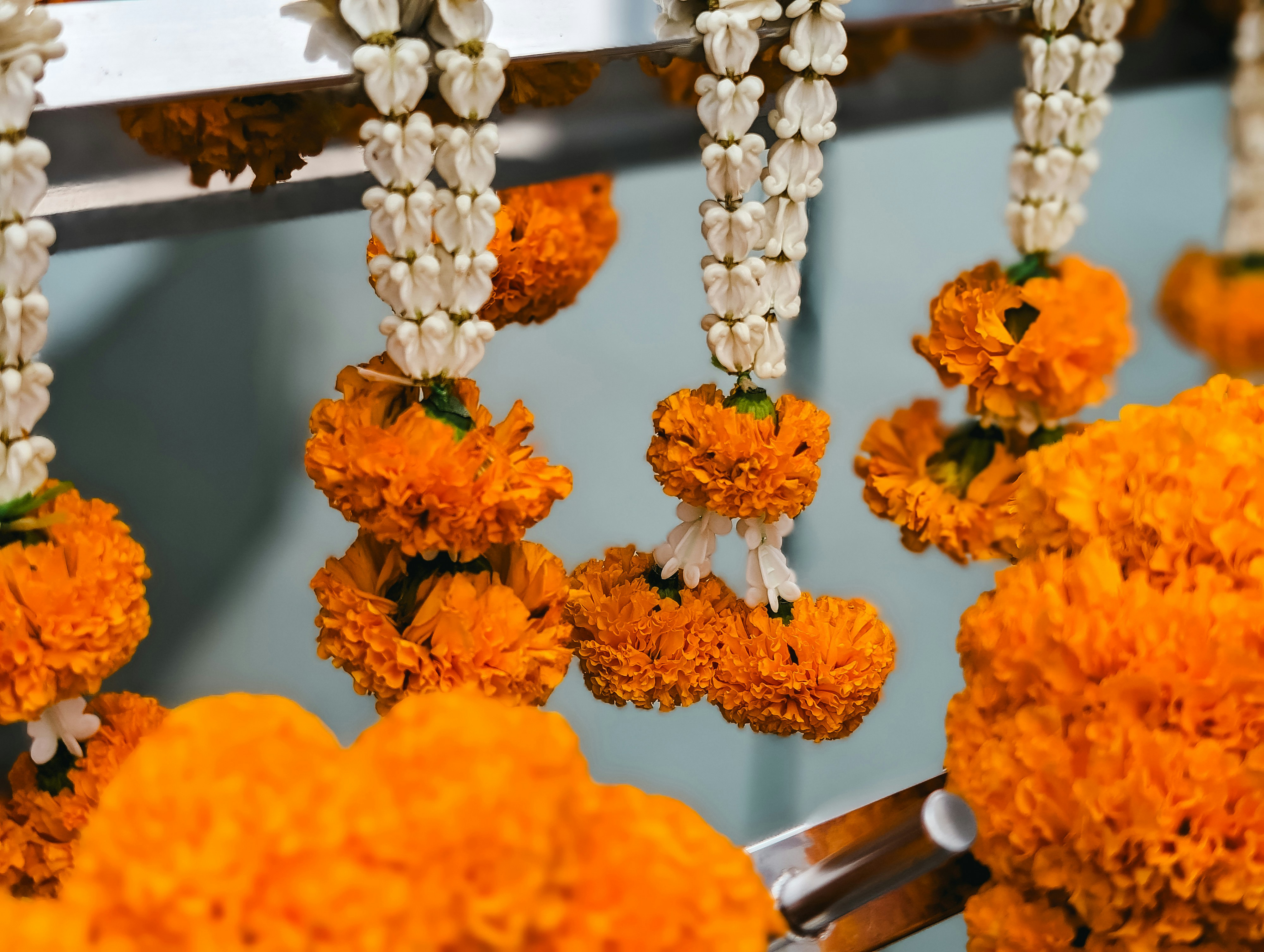 Orange marigold garlands and white jasmine strings hang in rows, filling the frame with bright fresh flowers.