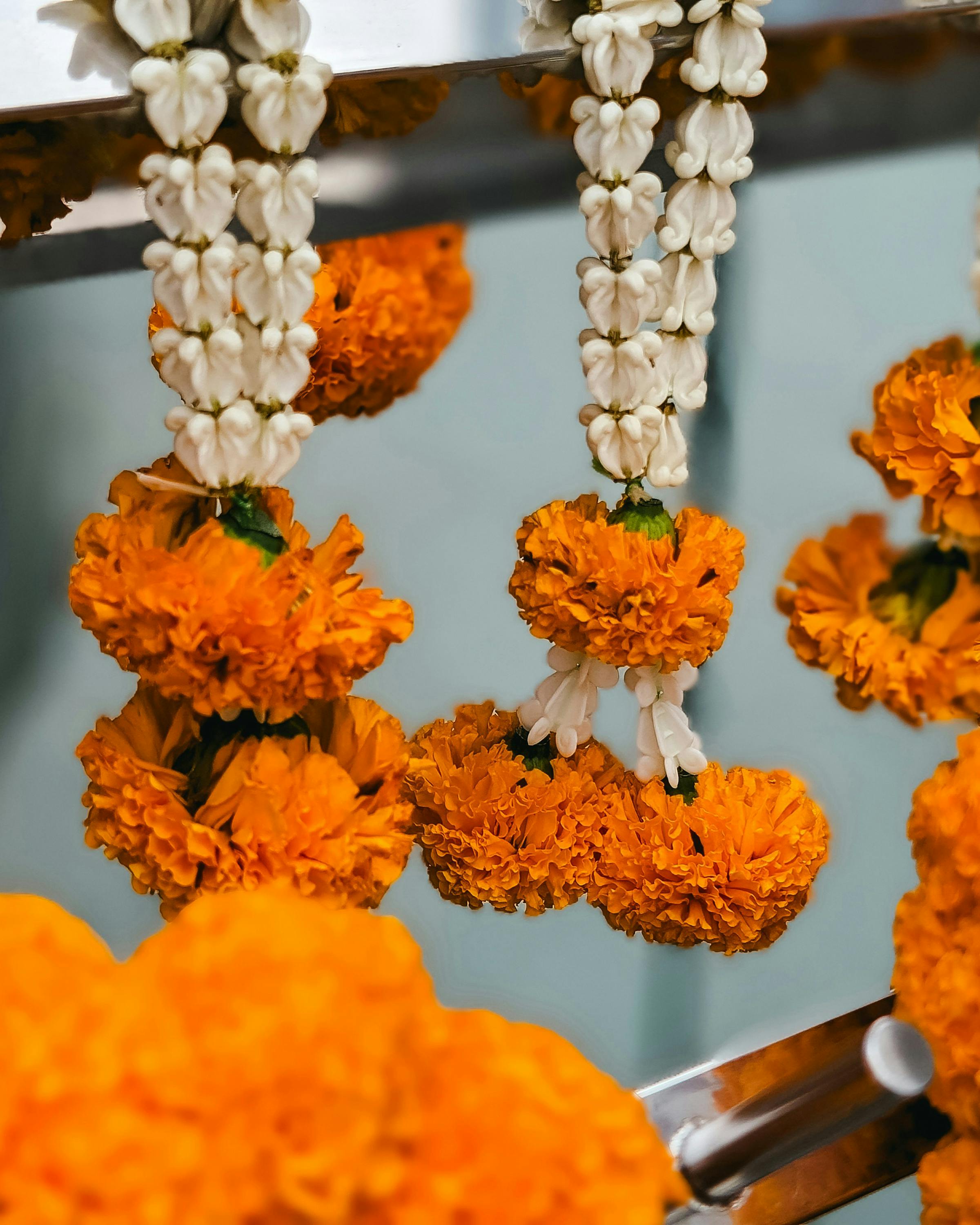 Orange marigold garlands and white jasmine strings hang in rows, filling the frame with bright fresh flowers.