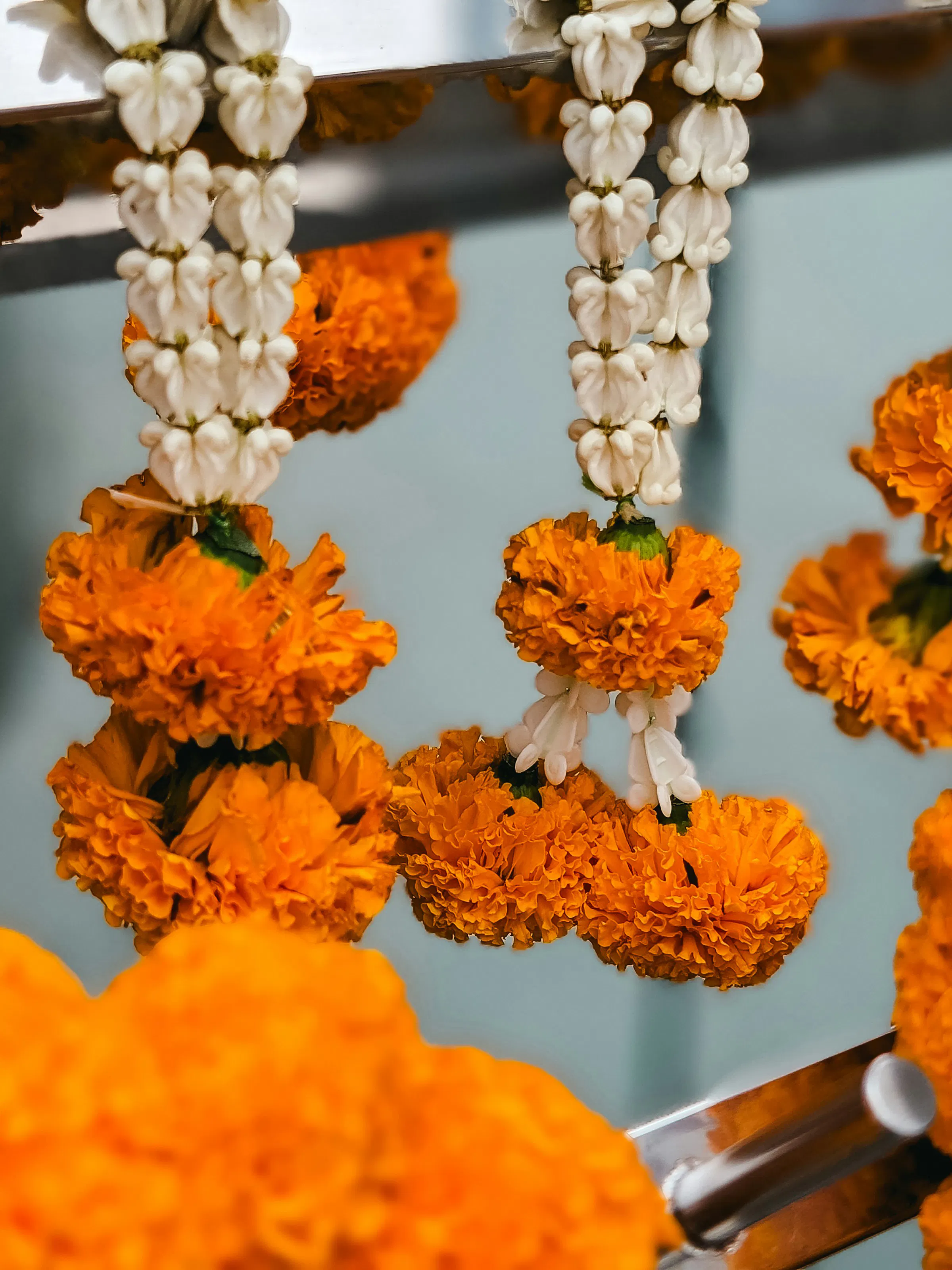 Orange marigold garlands and white jasmine strings hang in rows, filling the frame with bright fresh flowers.