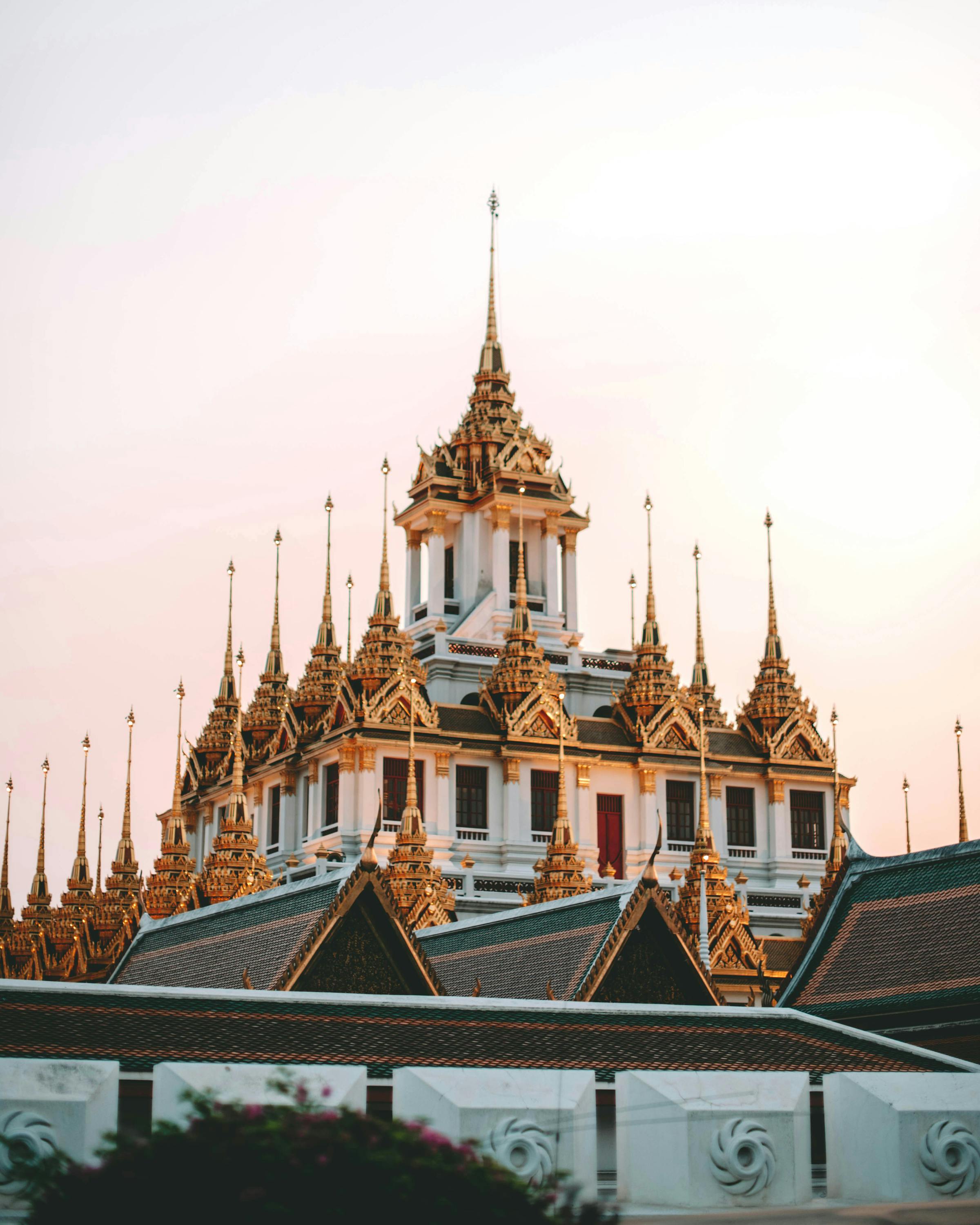 Golden spires and a tiled roof rise above a white wall at sunset, the sky fading from blue to pink behind.