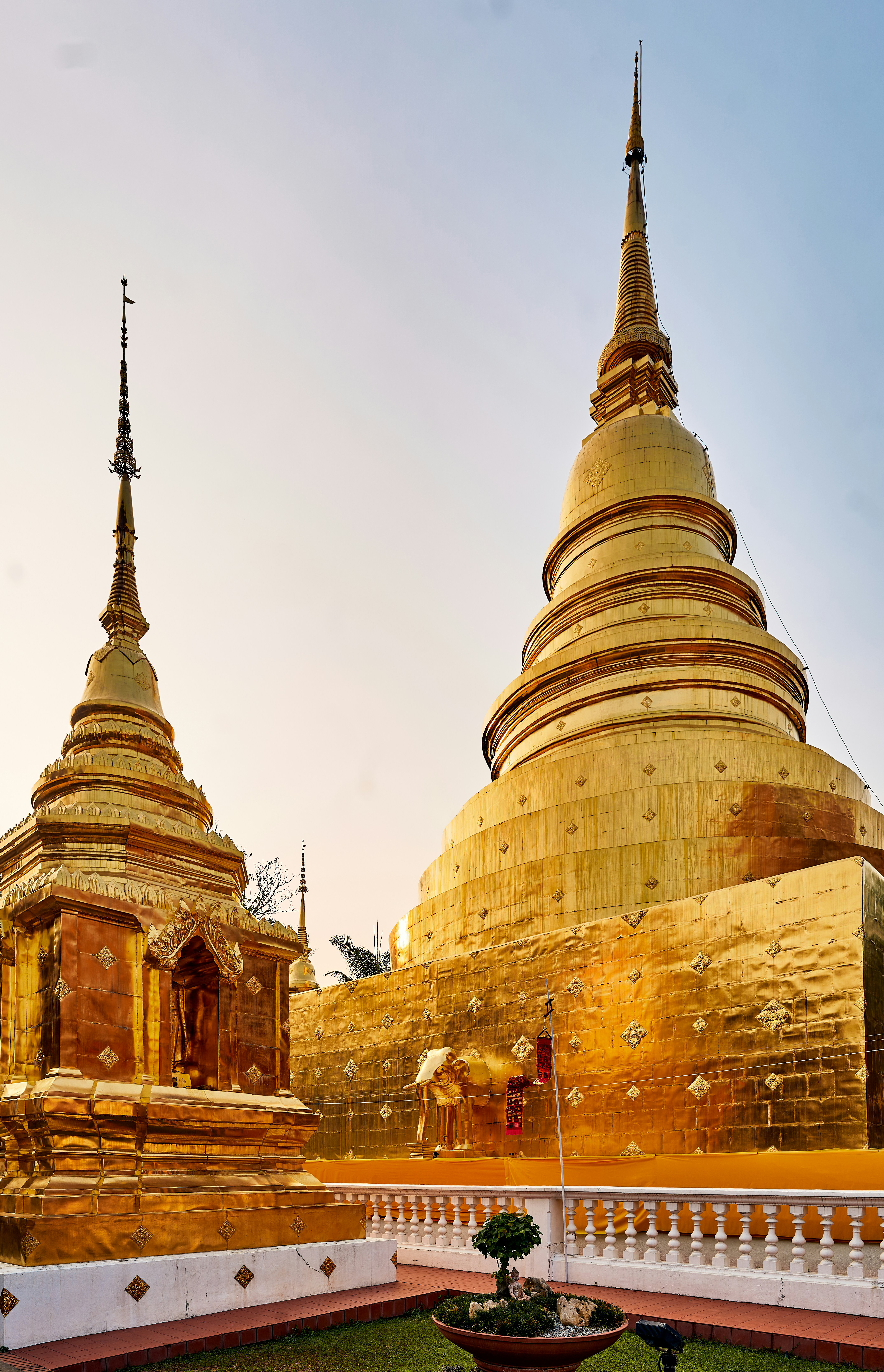 Golden temple stupas and spires gleam in soft evening light, with ornate details and tiled rooftops below.