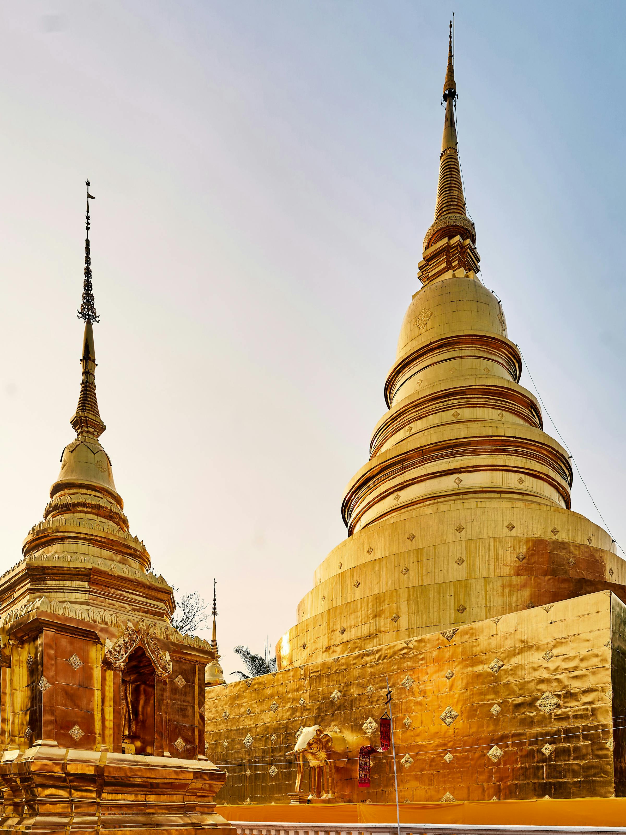 Golden temple stupas and spires gleam in soft evening light, with ornate details and tiled rooftops below.