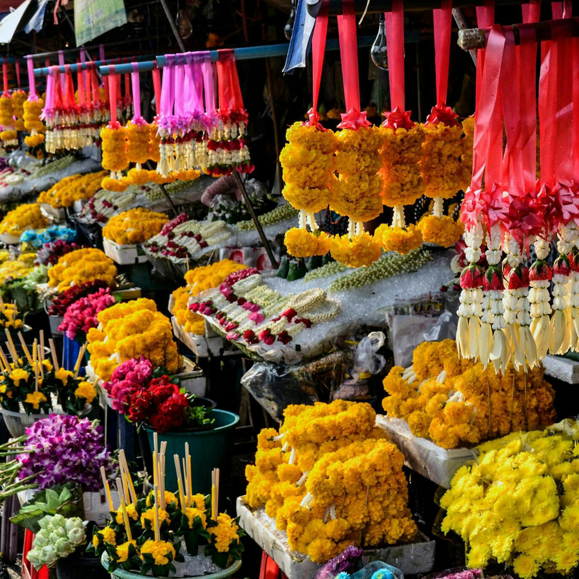 Bright flower market stall with hanging garlands and baskets of colorful blooms lined along a busy walkway.