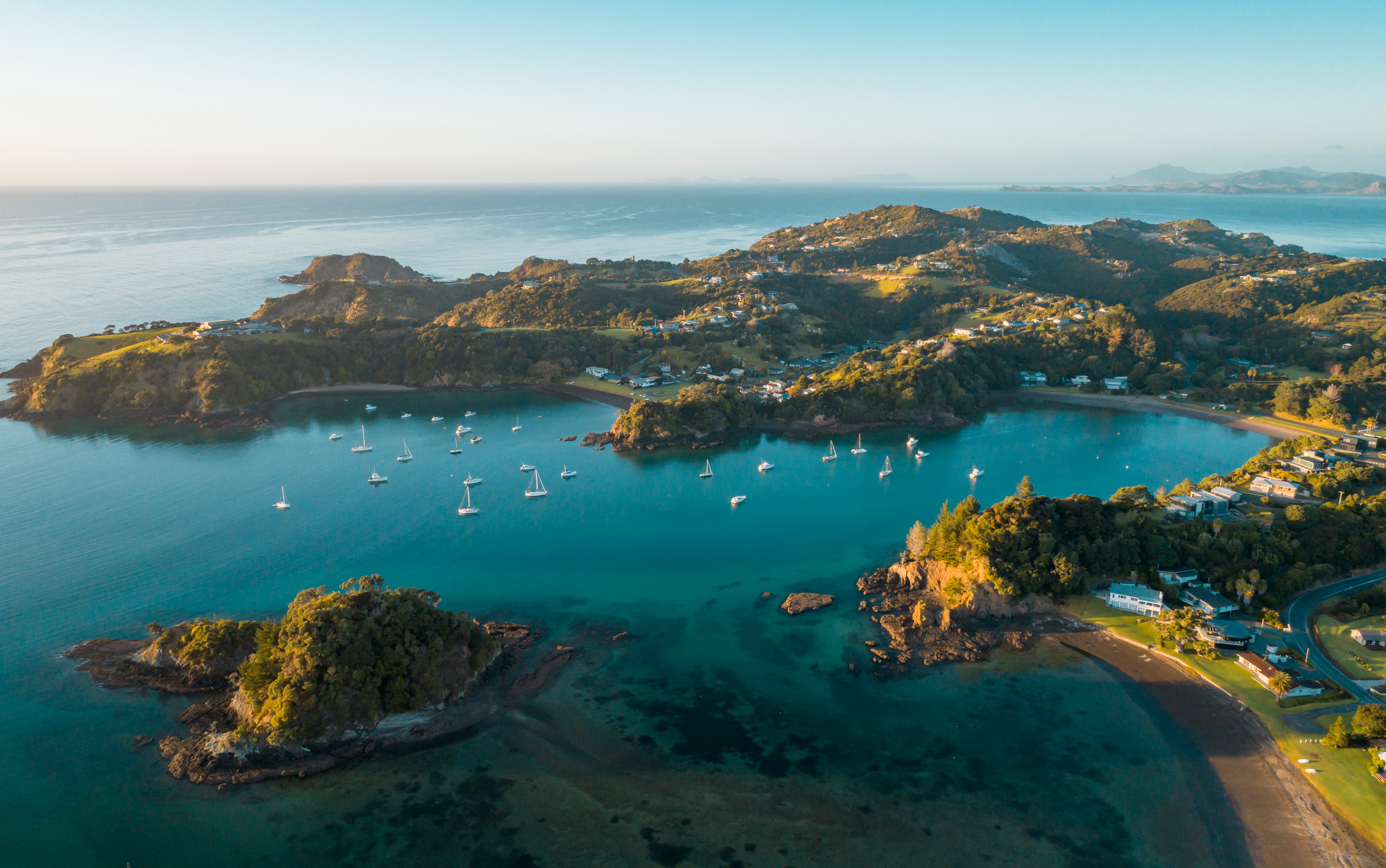 Aerial view of the Bay of Islands reveals turquoise inlets and many anchored boats around green headlands.