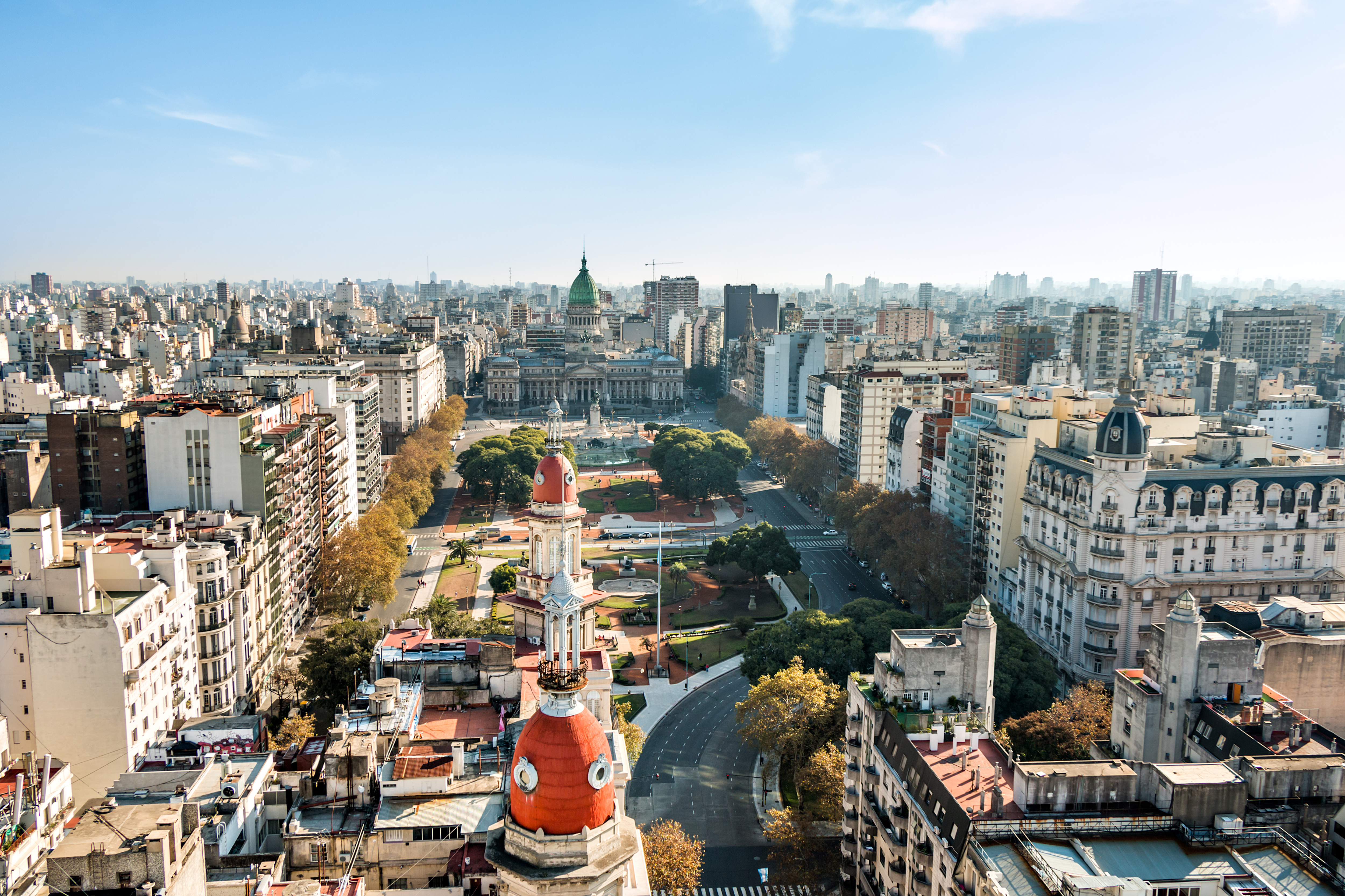 Aerial view of Buenos Aires shows a domed tower and broad avenue lined with buildings stretching toward the horizon.