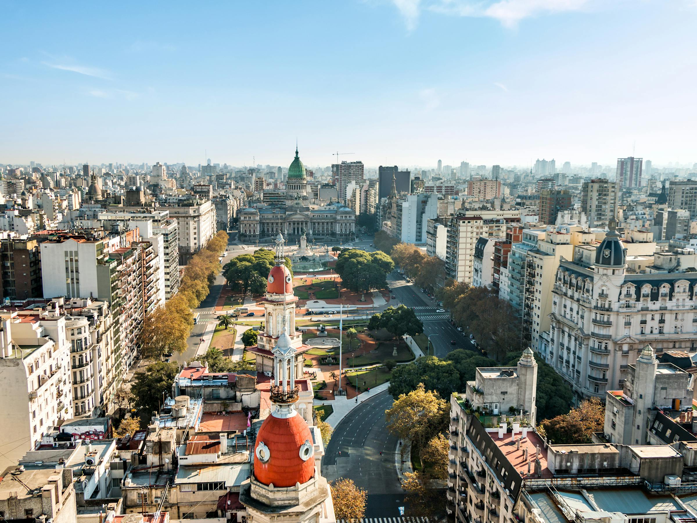 Aerial view of Buenos Aires shows a domed tower and broad avenue lined with buildings stretching toward the horizon.