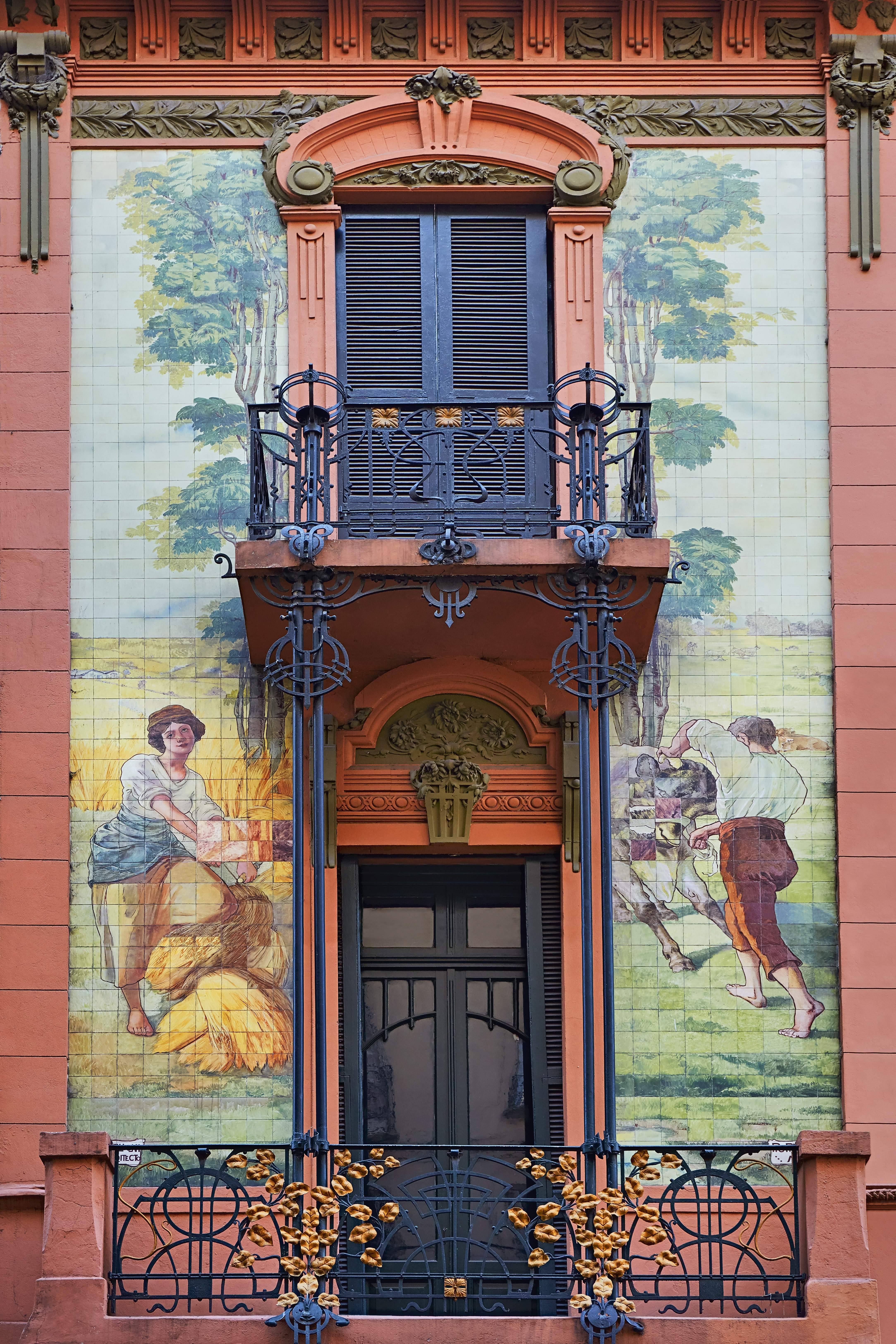 A colorful La Boca facade features painted murals and a wrought-iron balcony around a tall doorway in Buenos Aires.