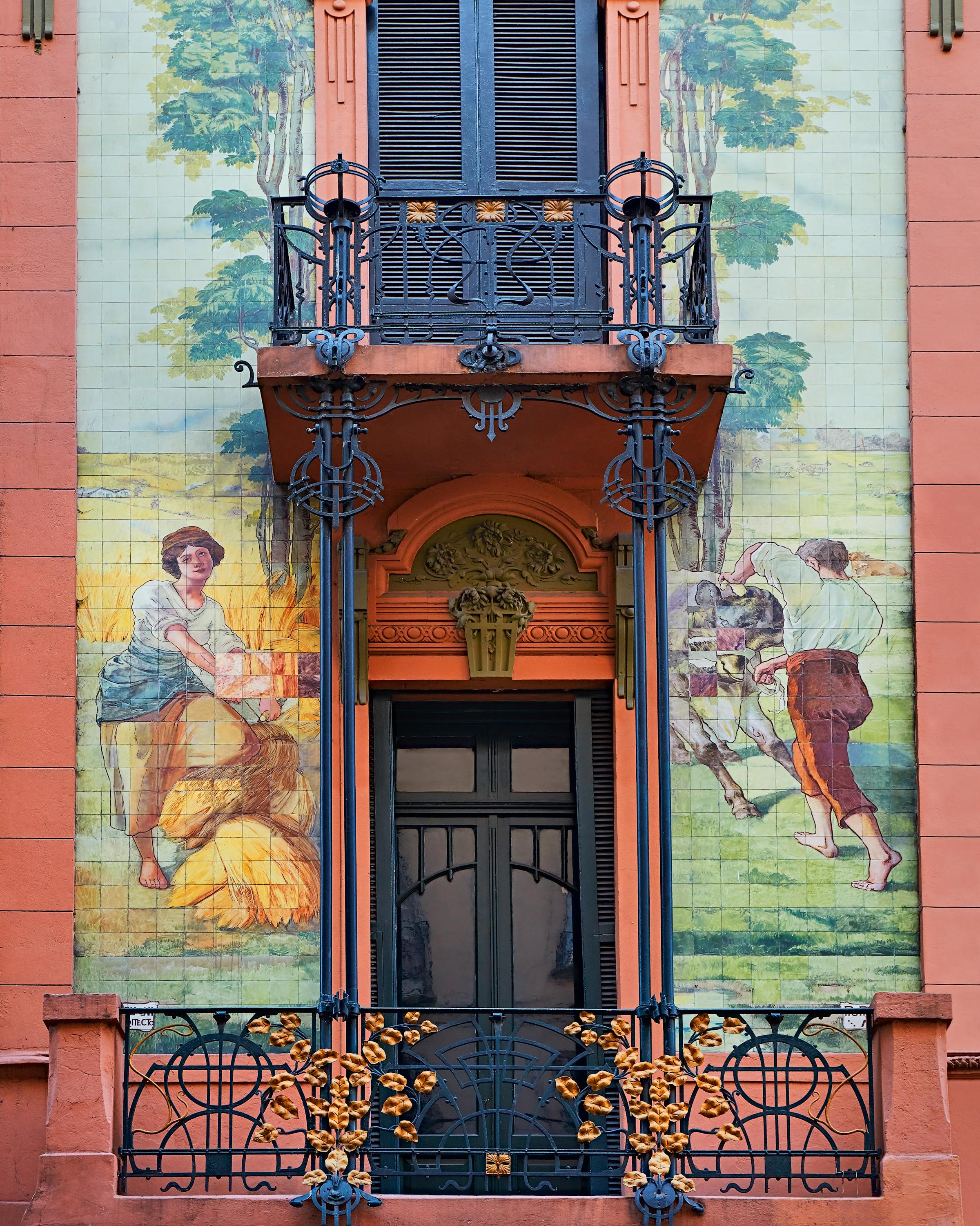 A colorful La Boca facade features painted murals and a wrought-iron balcony around a tall doorway in Buenos Aires.