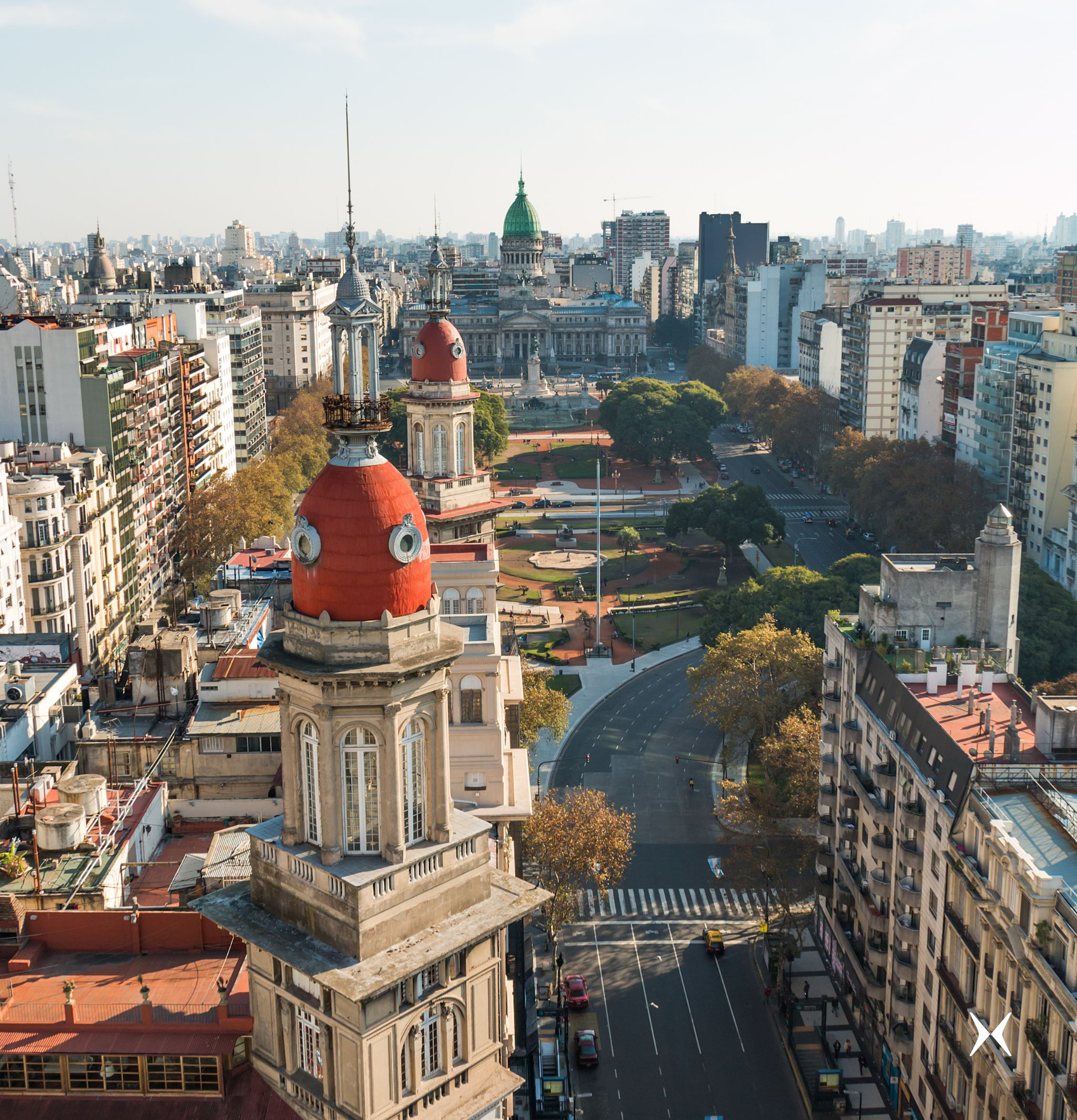 A domed building rises above a busy Buenos Aires boulevard, with city blocks and distant skyline under clear light.