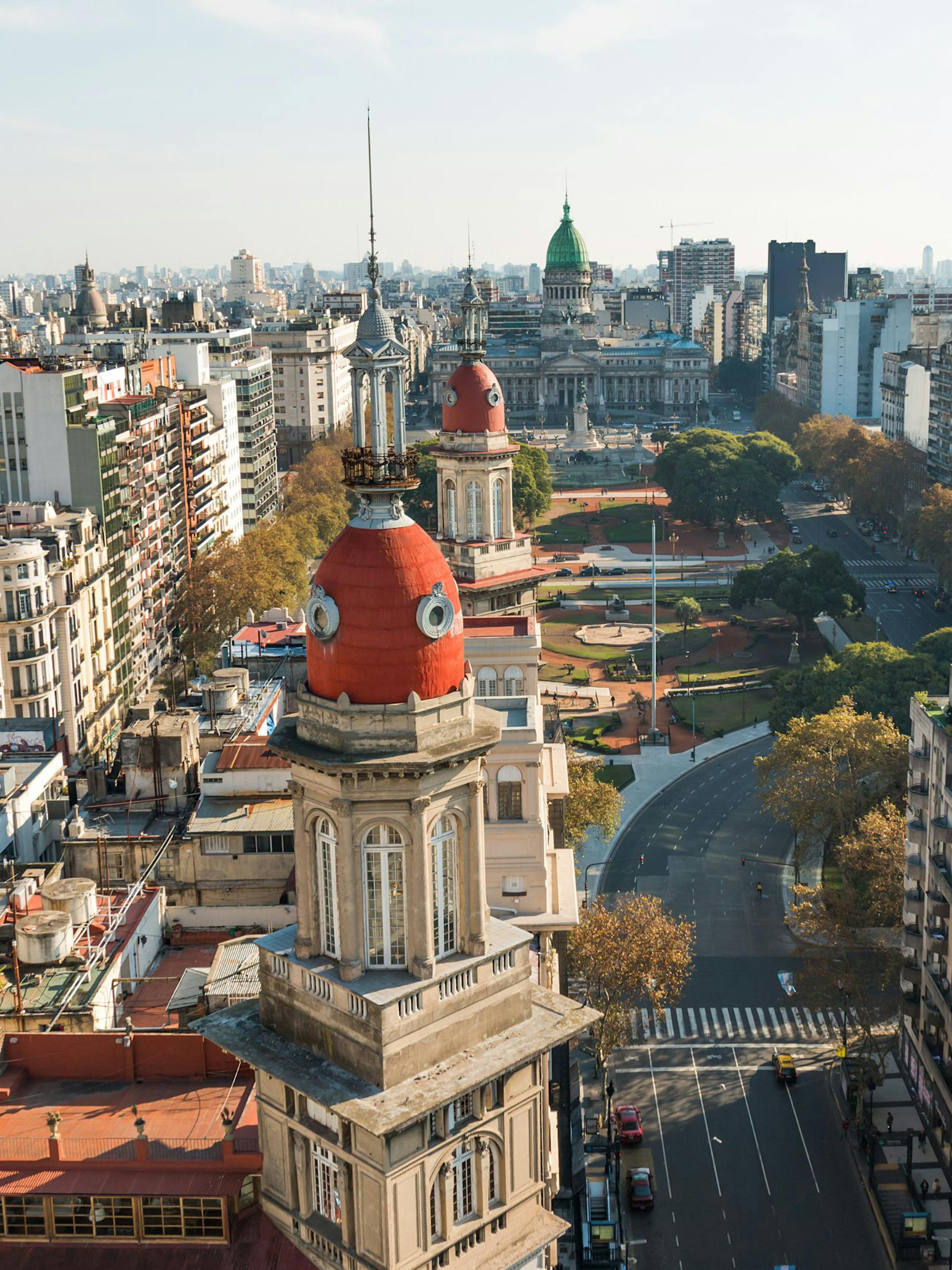 A domed building rises above a busy Buenos Aires boulevard, with city blocks and distant skyline under clear light.