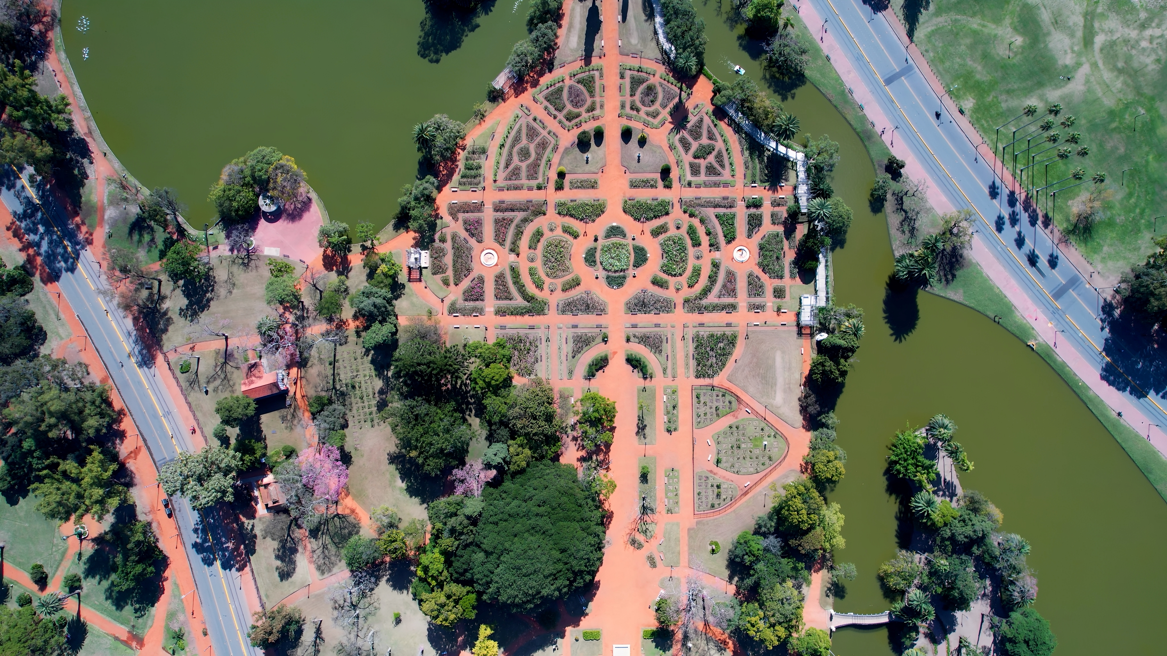 Aerial view of a formal rose garden shows curved paths and geometric beds surrounded by trees in Buenos Aires parkland.