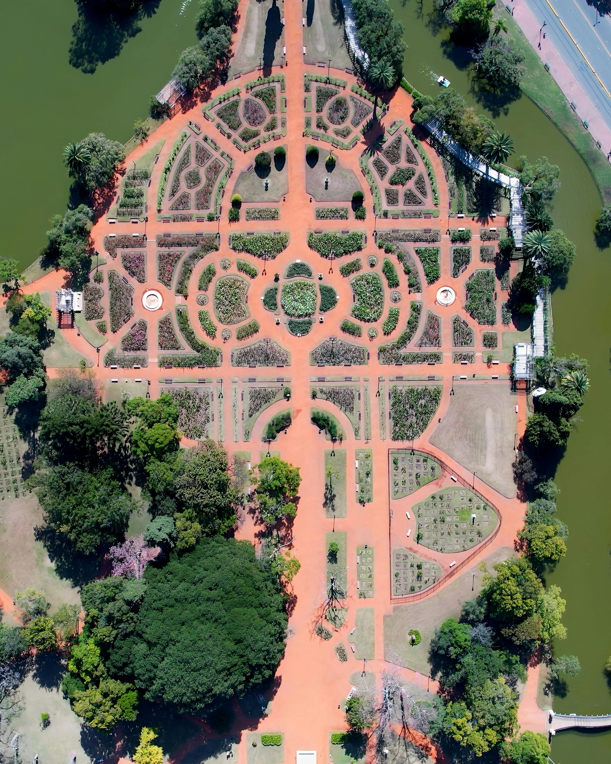Aerial view of a formal rose garden shows curved paths and geometric beds surrounded by trees in Buenos Aires parkland.