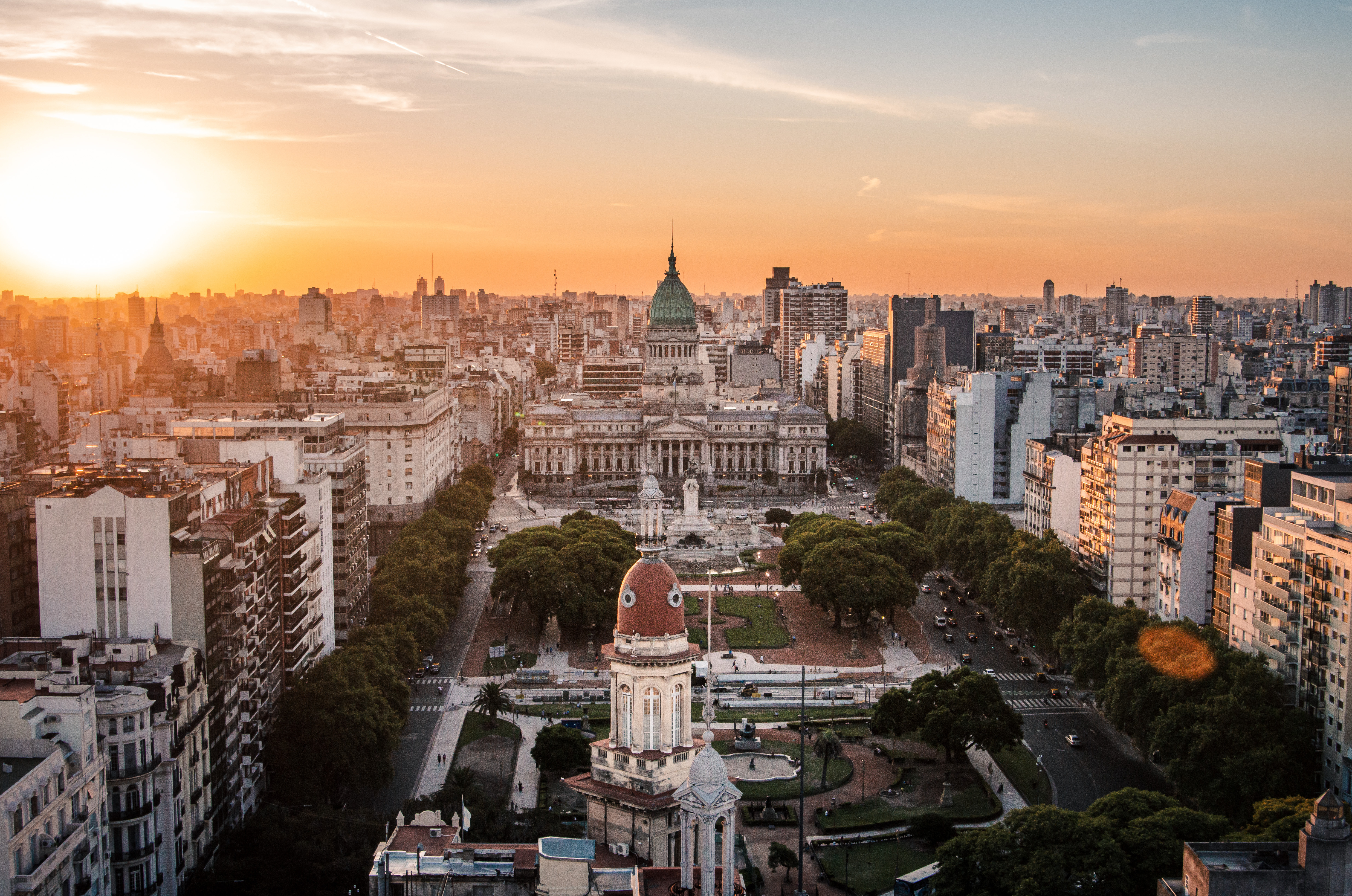 Sunset light washes over Buenos Aires, with the Congress building and domed rooftops above tree-lined streets and parks.