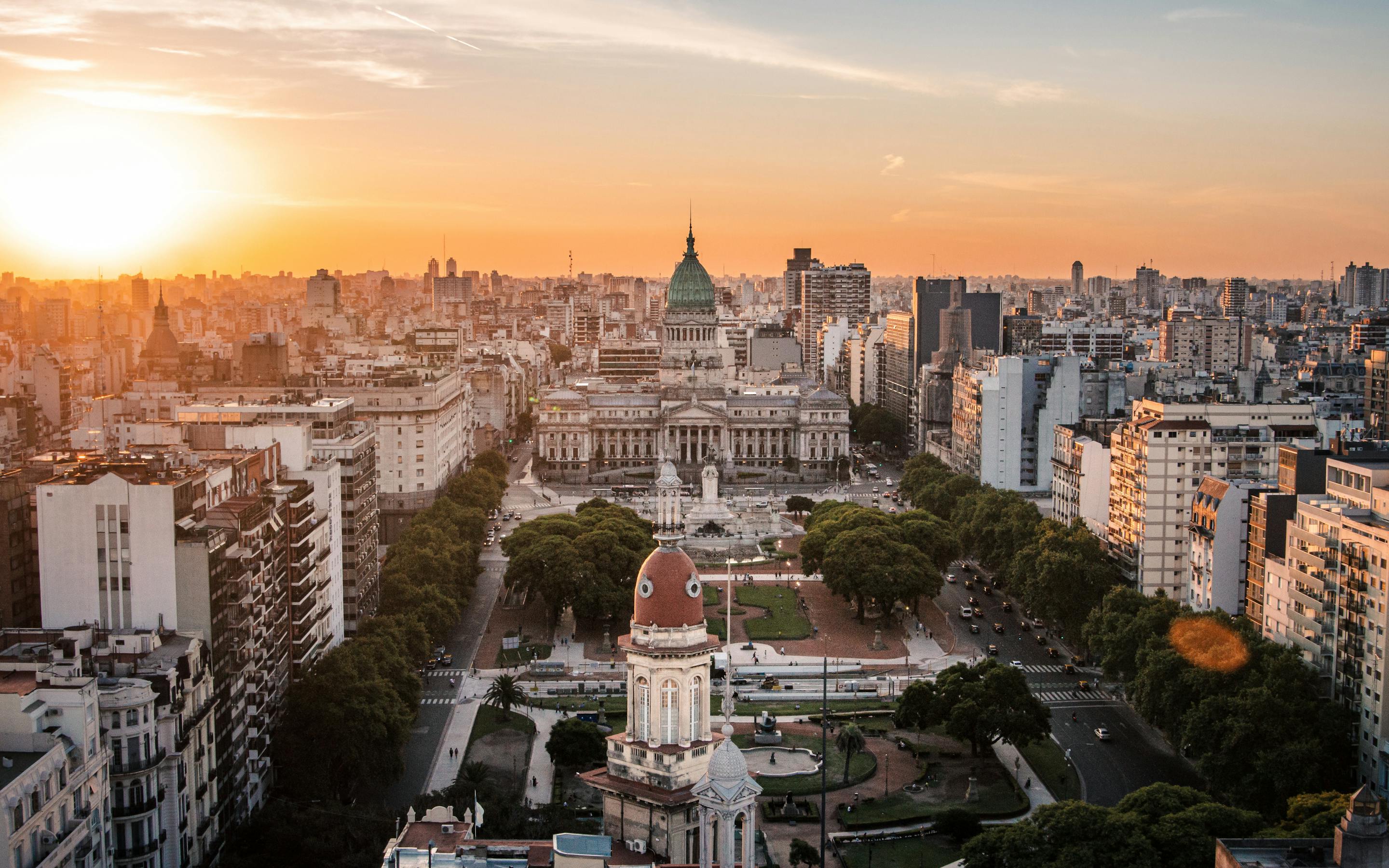 Sunset light washes over Buenos Aires, with the Congress building and domed rooftops above tree-lined streets and parks.