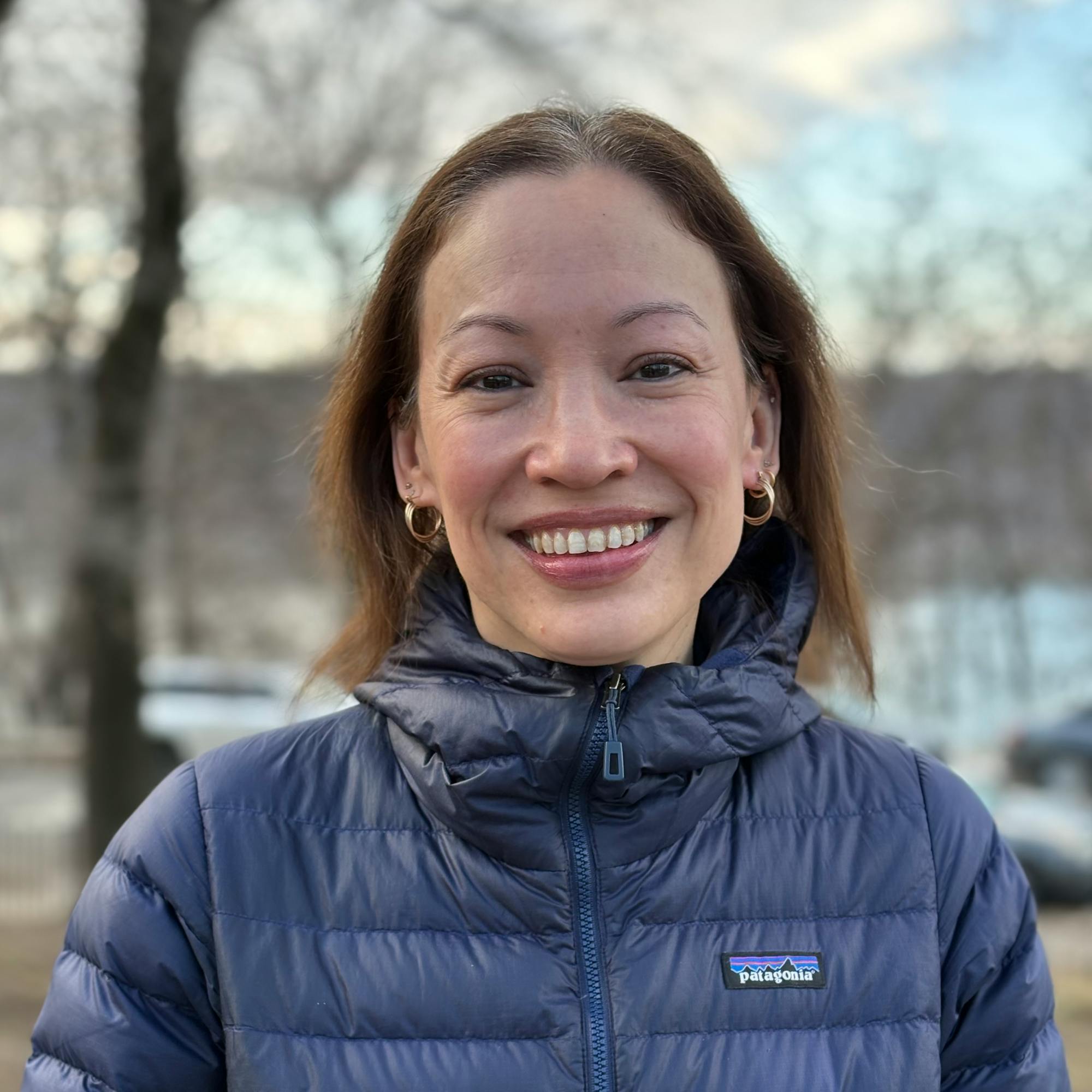 Headshot of a smiling woman wearing a blue jacket and standing outdoors.