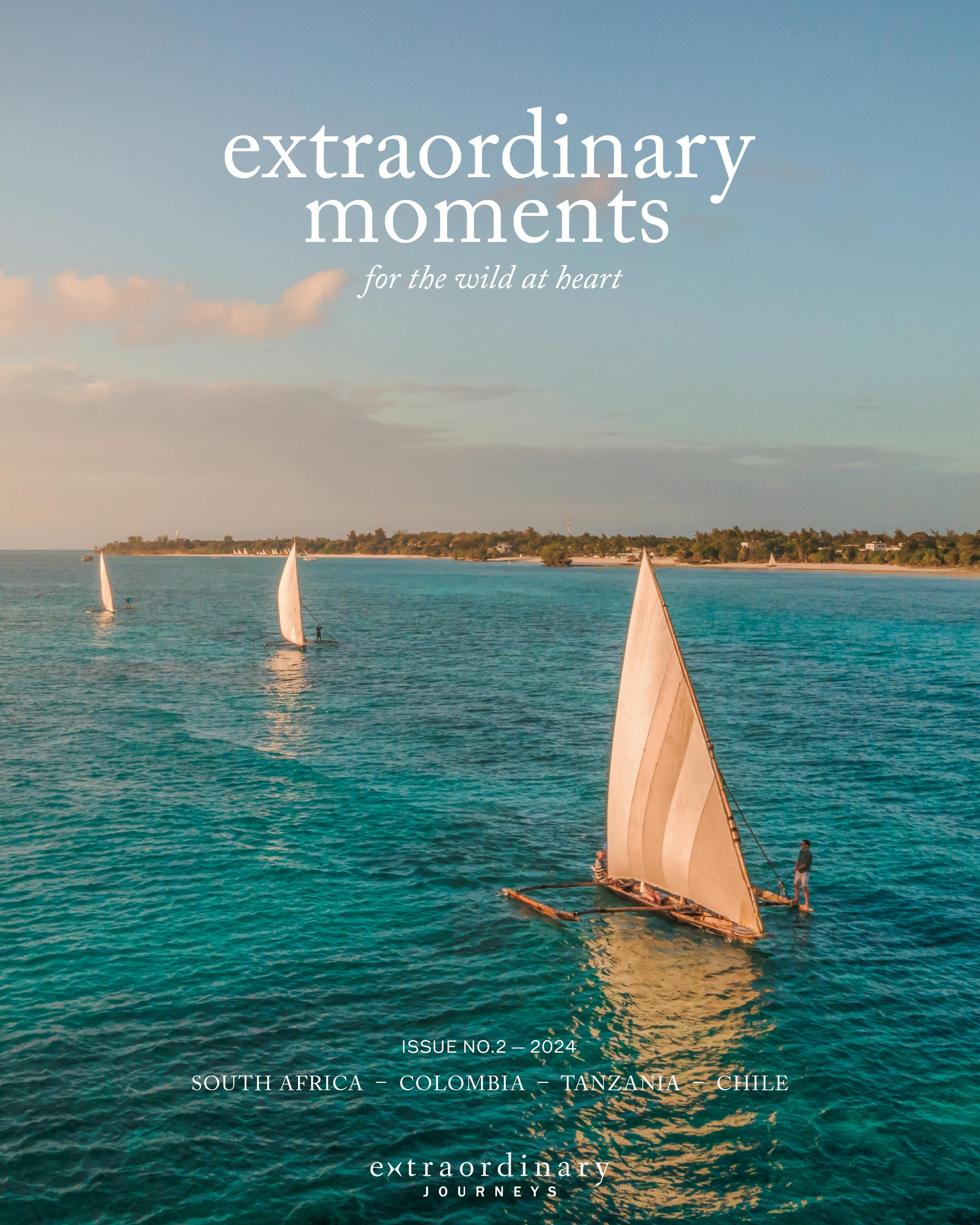 Traditional wooden sailboats glide across turquoise ocean water near a tropical coastline at sunset. Cover text reads: “extraordinary moments – for the wild at heart.”