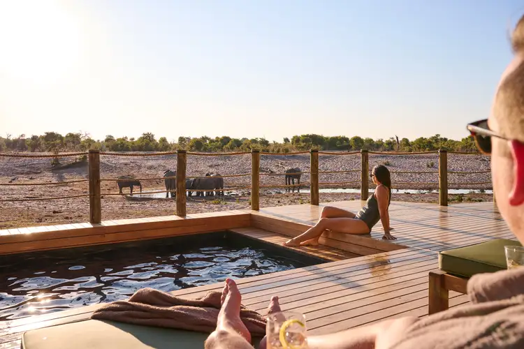 Two people in swimsuits lay by a pool, with wildlife in the distance.