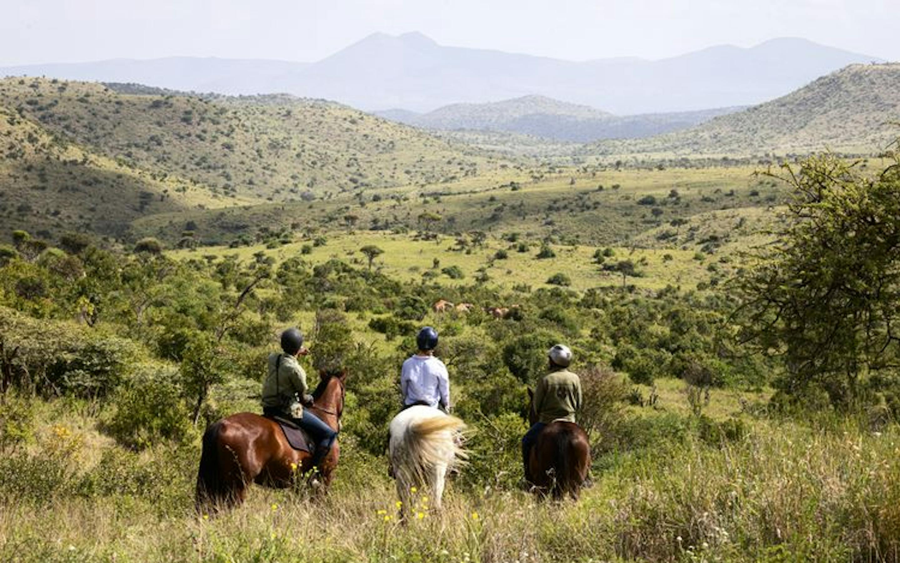 Three people on horseback look out over a vast plain in Kenya.