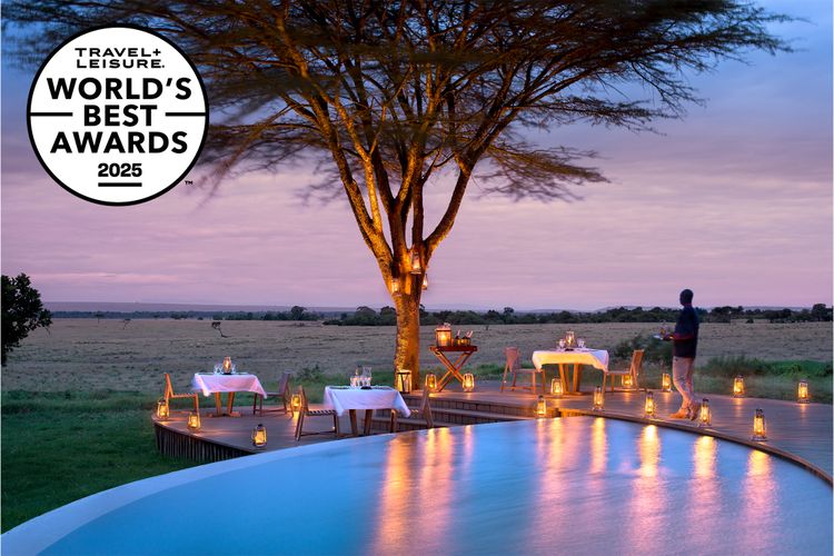 An infinity pool overlooks an open savanna at sunset, where lantern-lit dining tables are set beneath a large tree. A circular badge in the corner reads “Travel + Leisure World’s Best Awards 2025.”