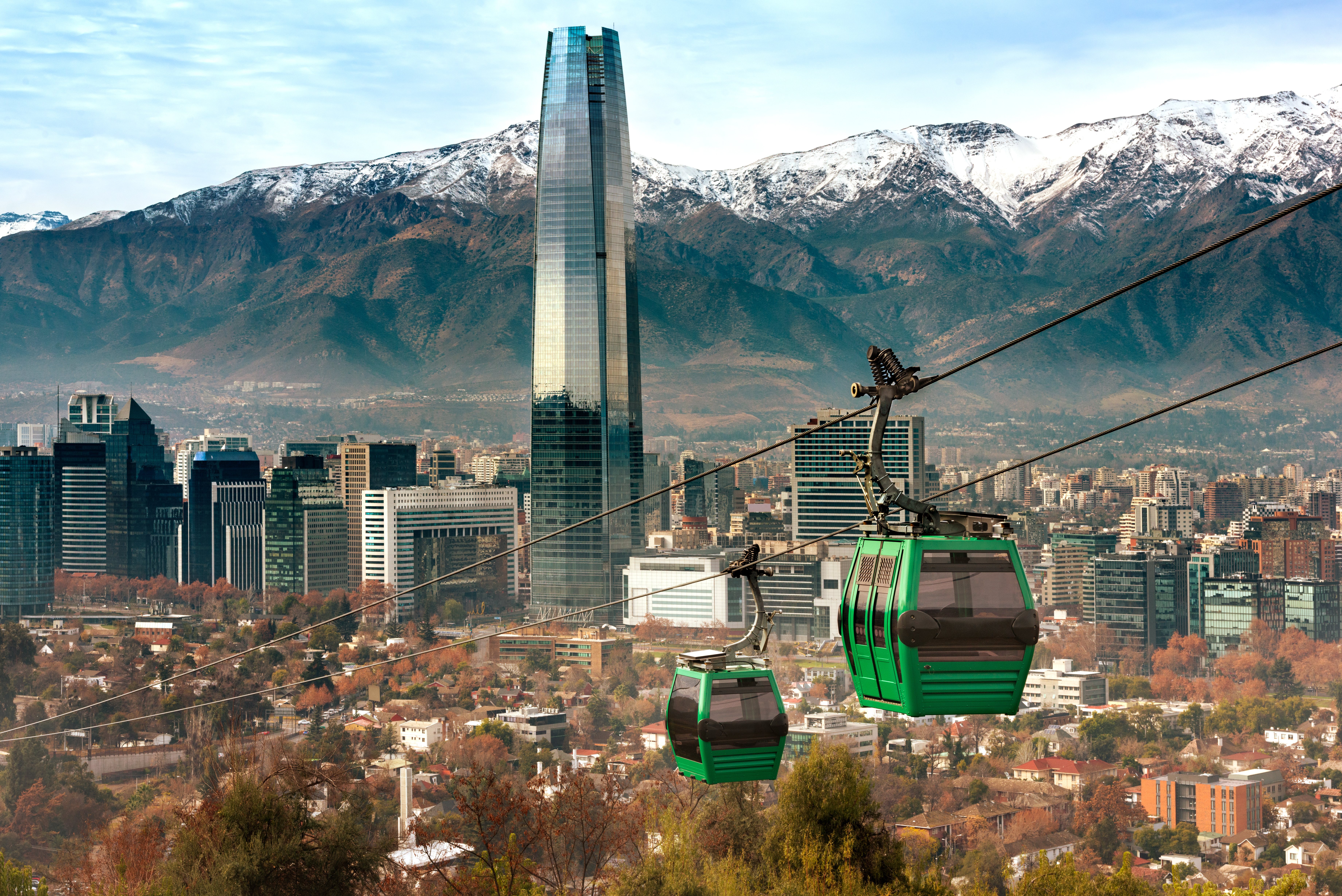 Green cable cars glide above Santiago toward the Andes, with high-rises below and snowy peaks behind them.
